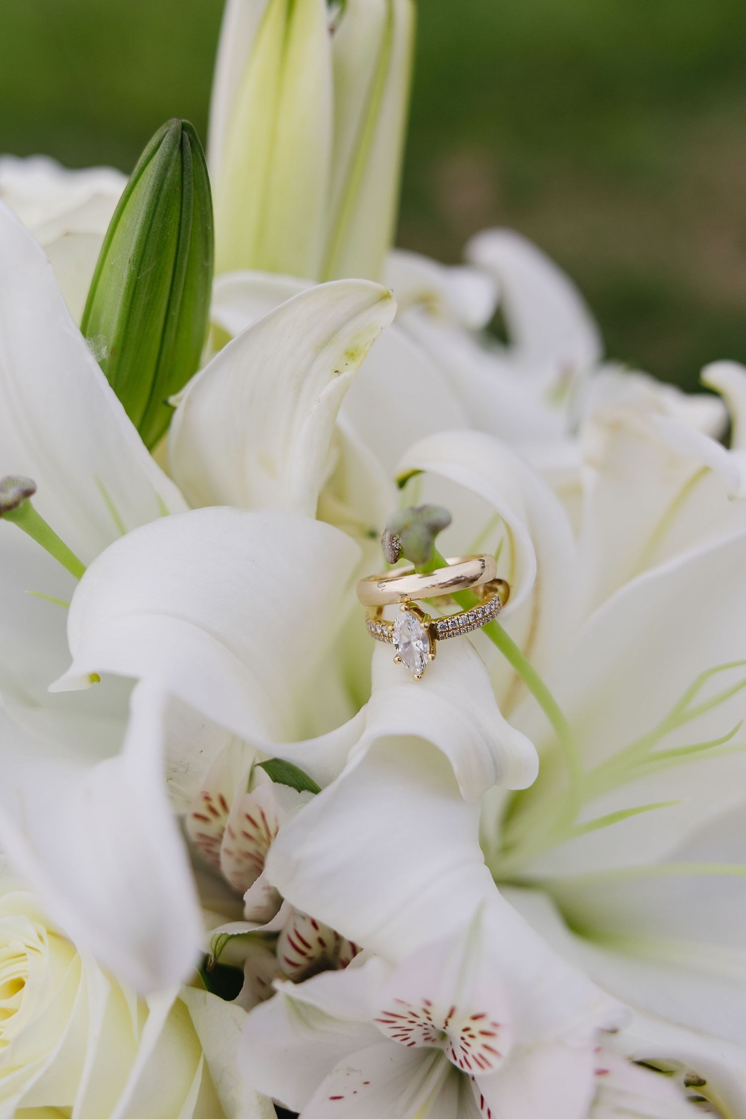 Close-up of gold wedding rings and diamond engagement ring nestled in white lily bridal bouquet.