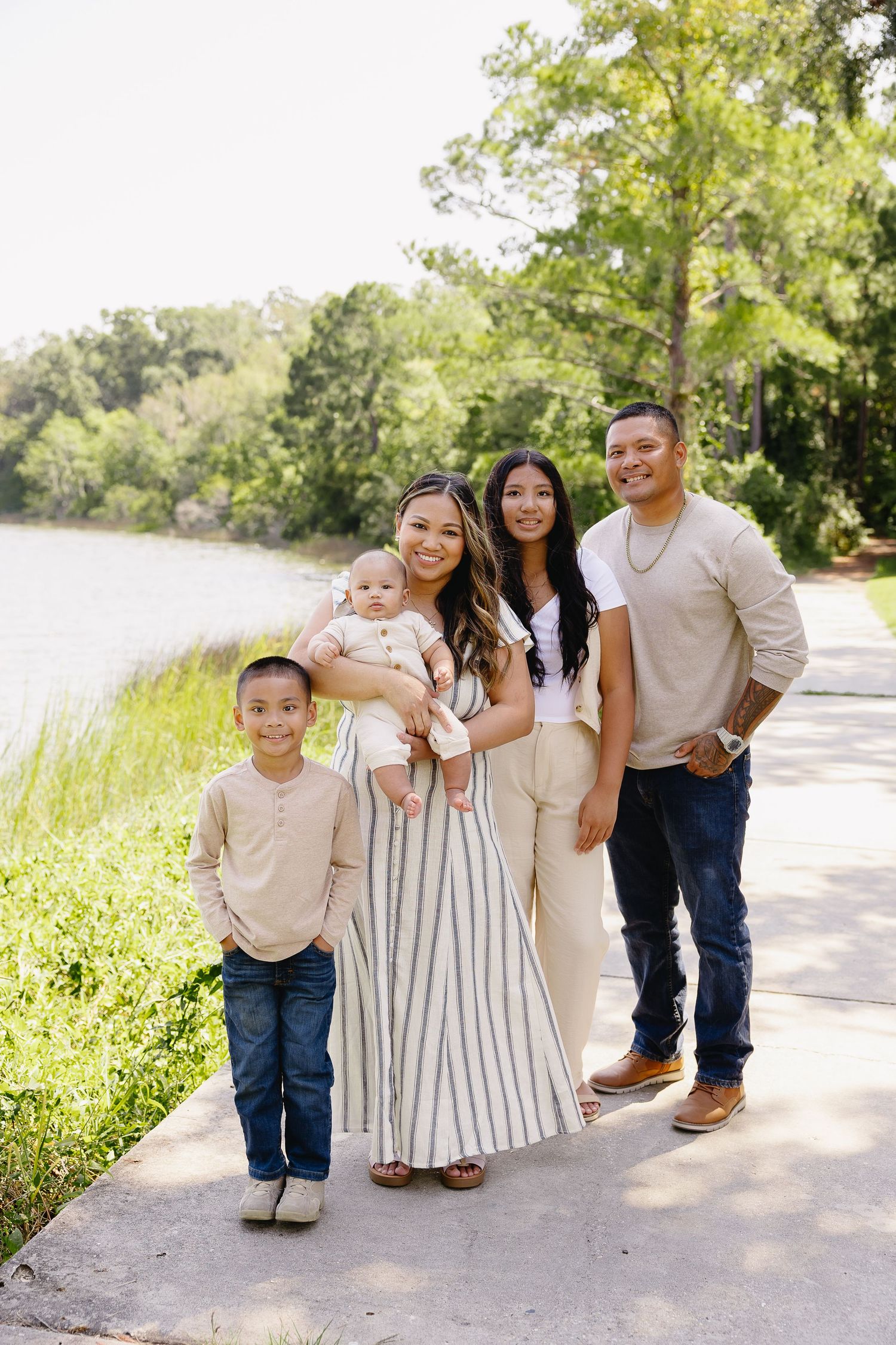 Cheerful family of five posing on a lakeside path surrounded by lush greenery.