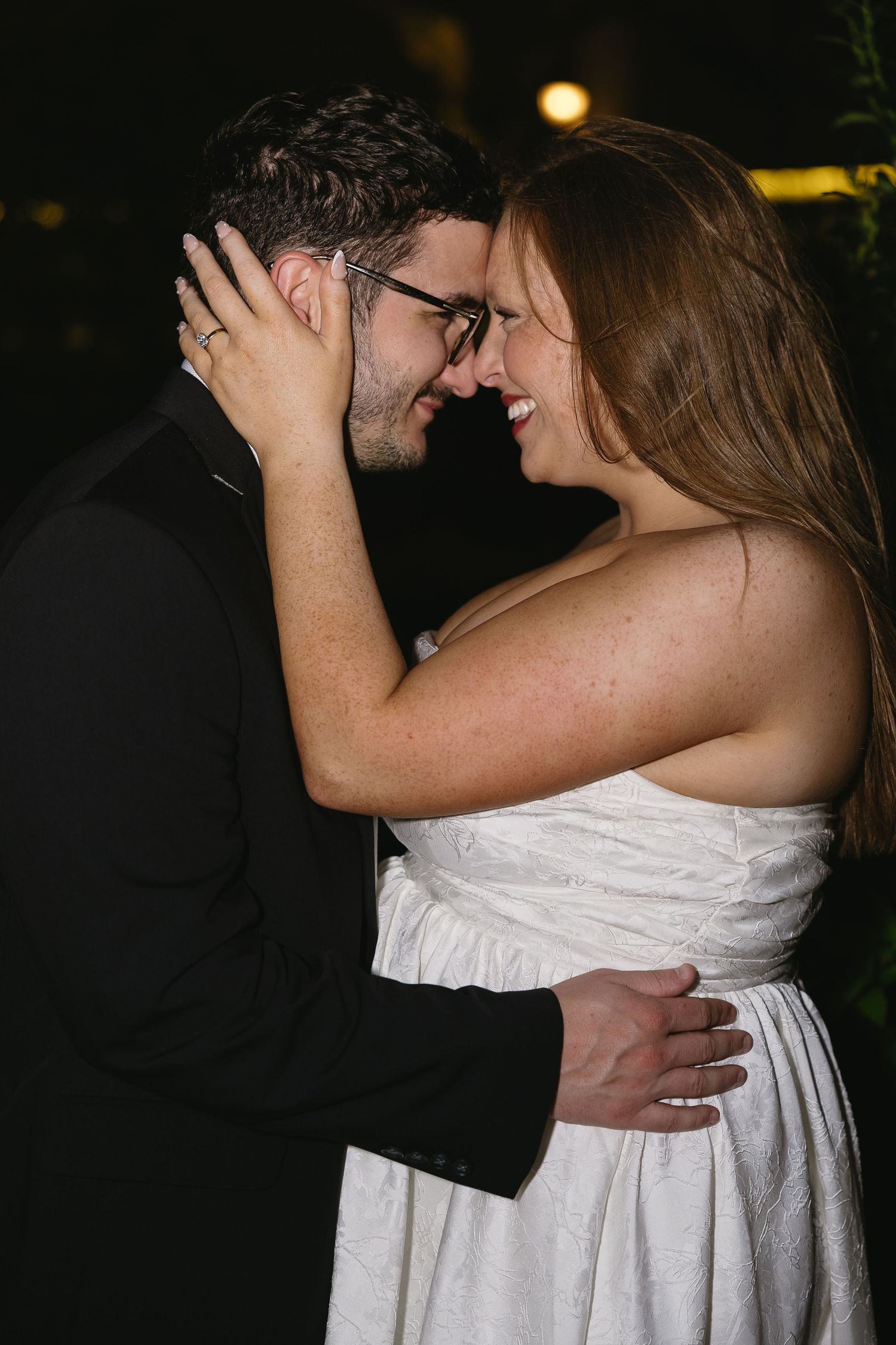 Laughing bride and groom touching foreheads in intimate embrace during romantic nighttime photo.