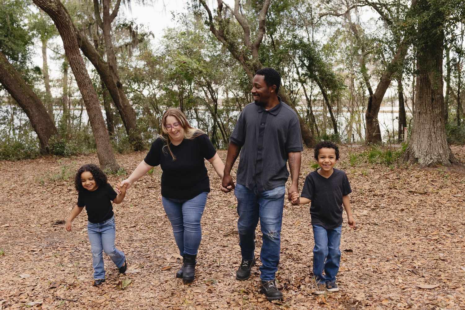 A happy family of four walking hand in hand through a leafy outdoor park setting.