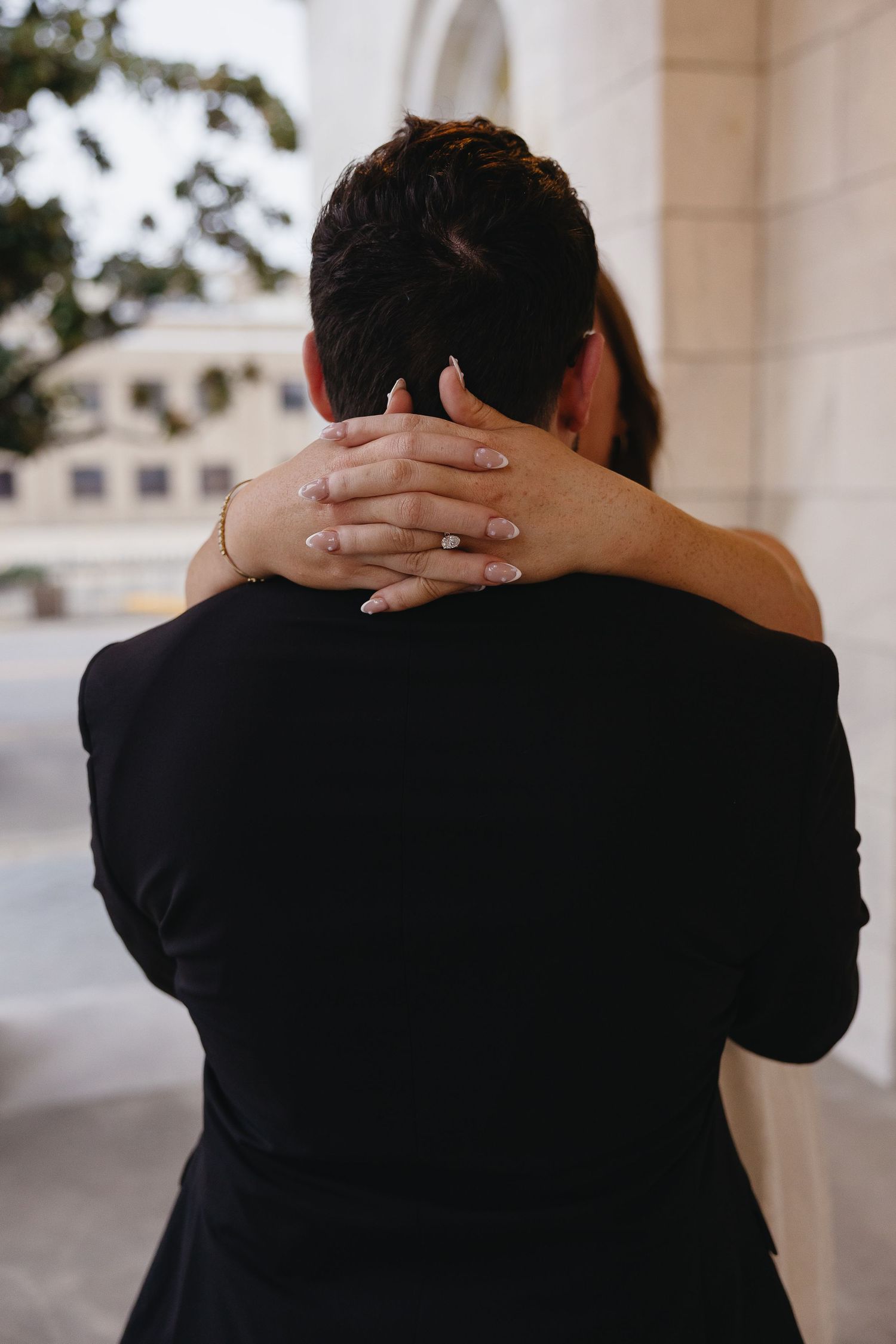 A woman wraps her hands around a mans neck from behind in a tender romantic embrace.