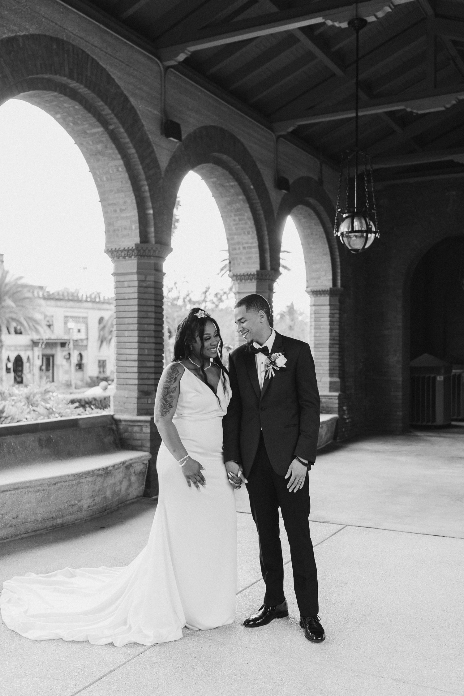 Black and white photo of bride and groom laughing under brick arched venue.