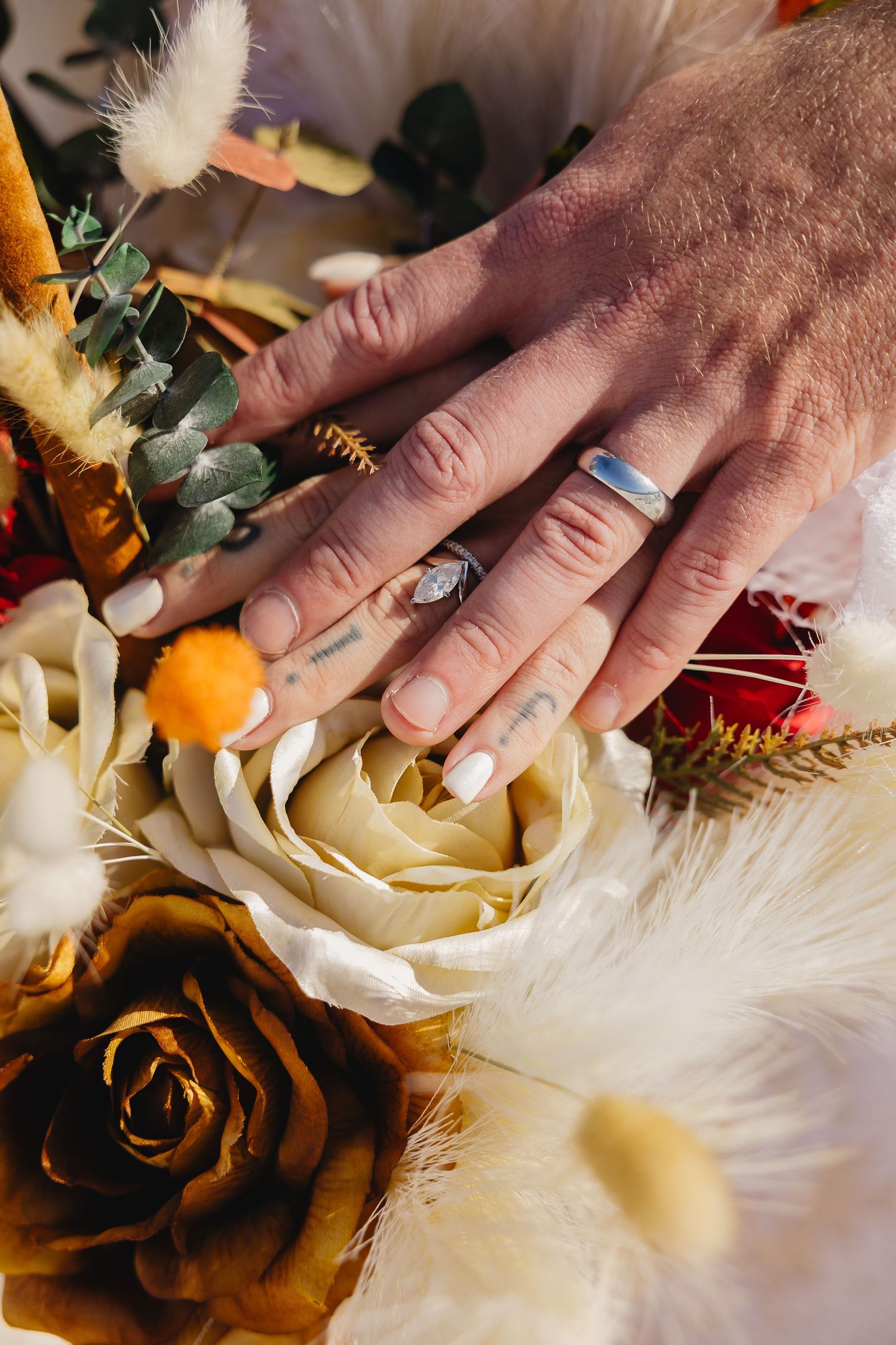 Newlyweds display wedding rings over a boho bouquet of roses and dried flowers.