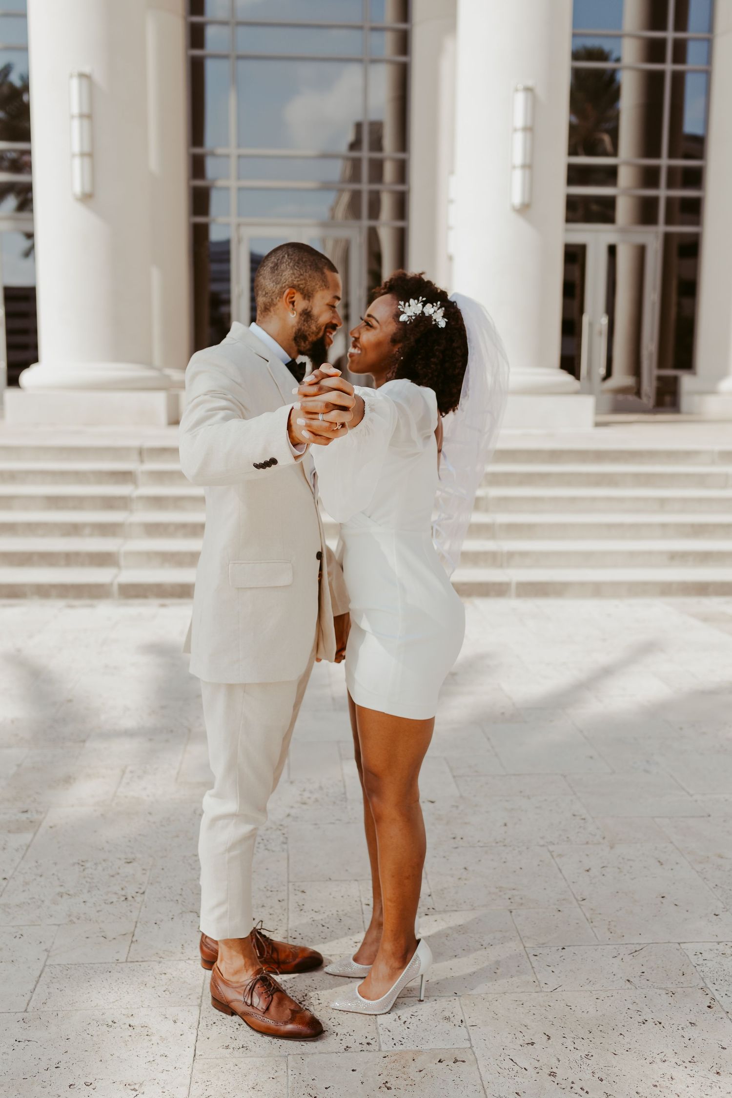 Bride and groom dancing together in front of a white columned building on their wedding day.