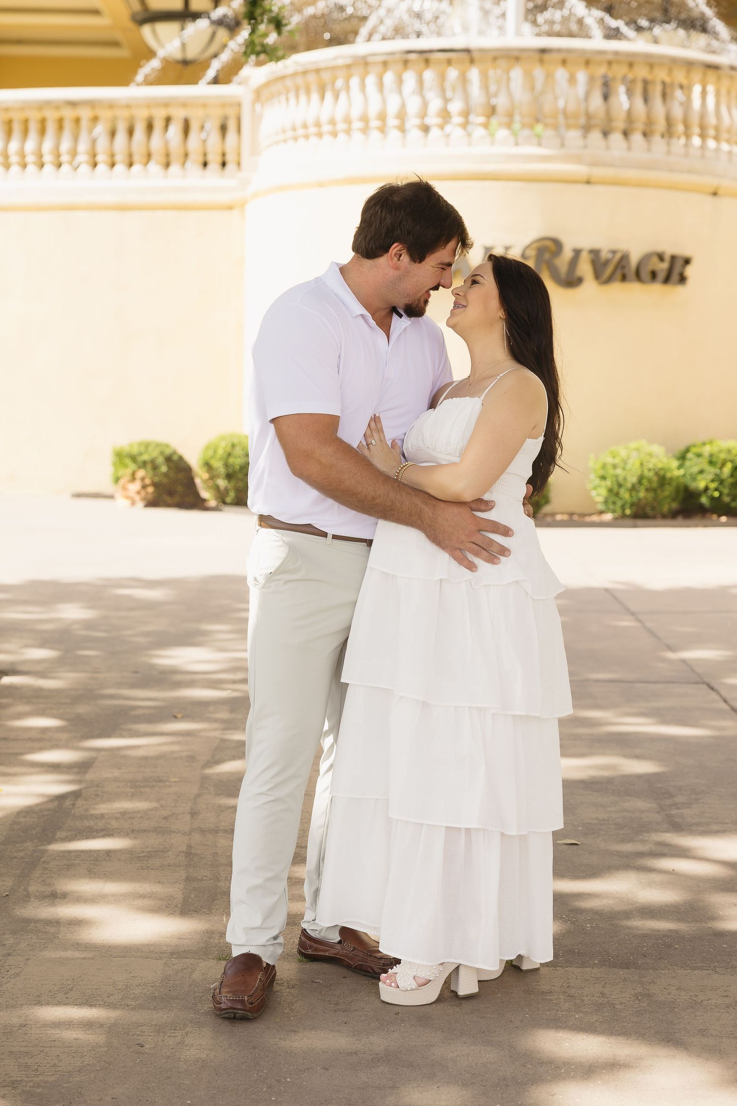 Expecting couple embracing and touching foreheads in front of the Beau Rivage resort fountain.
