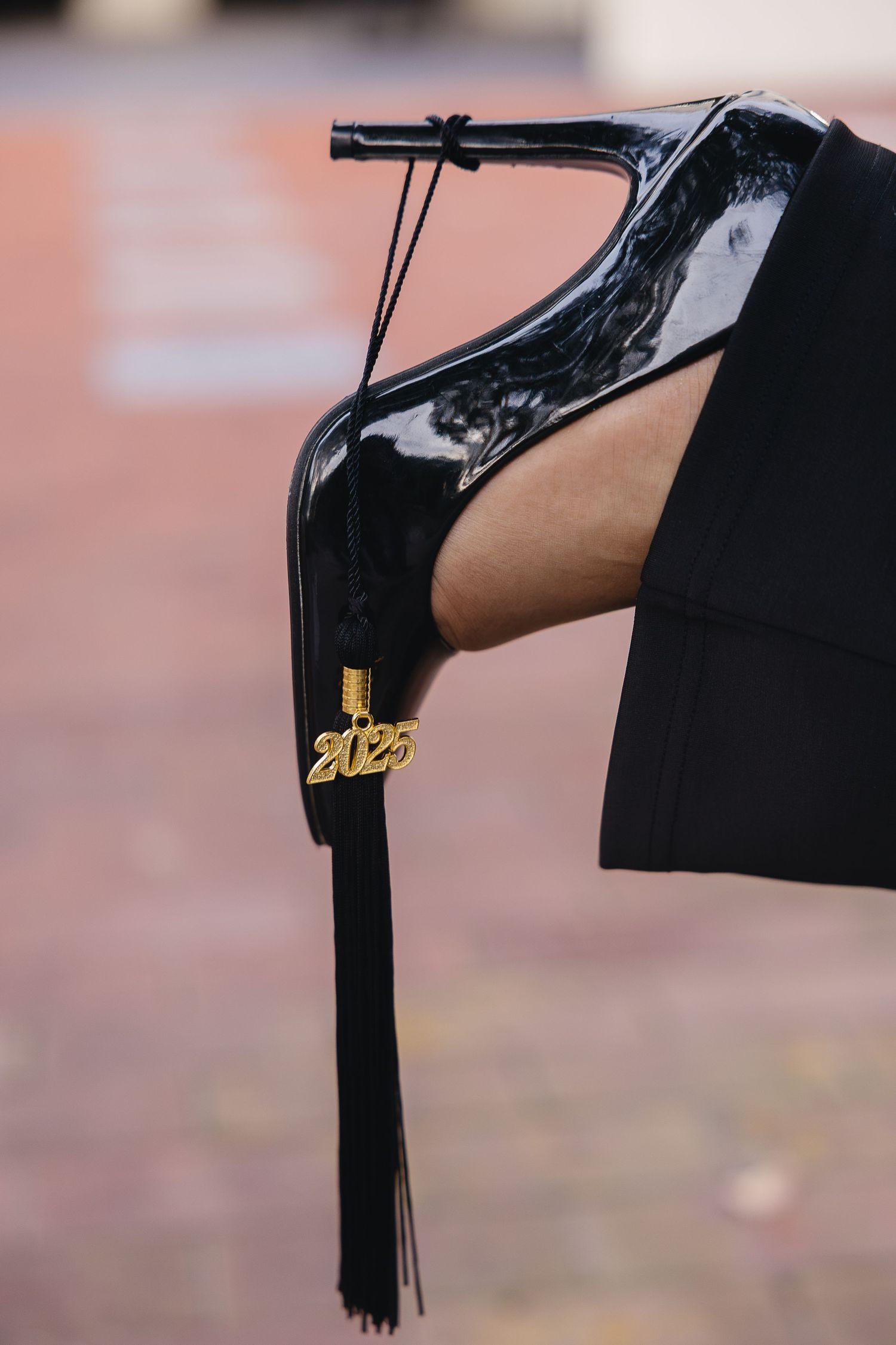 A close-up of a black patent heel with a gold 2025 graduation tassel charm attached.
