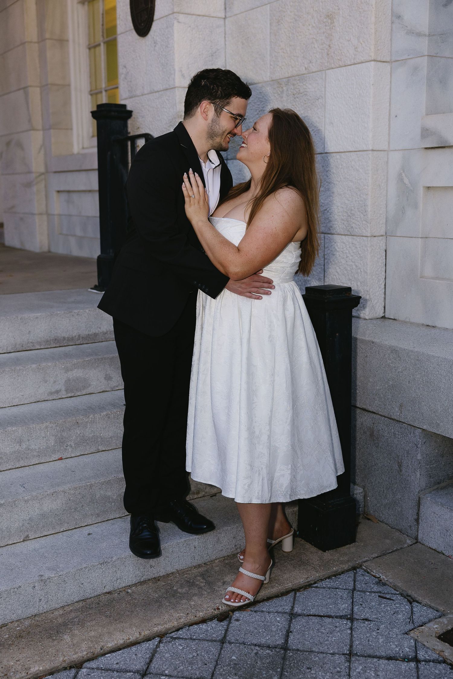 Newlyweds sharing romantic moment, nearly kissing while standing close together on stone steps.