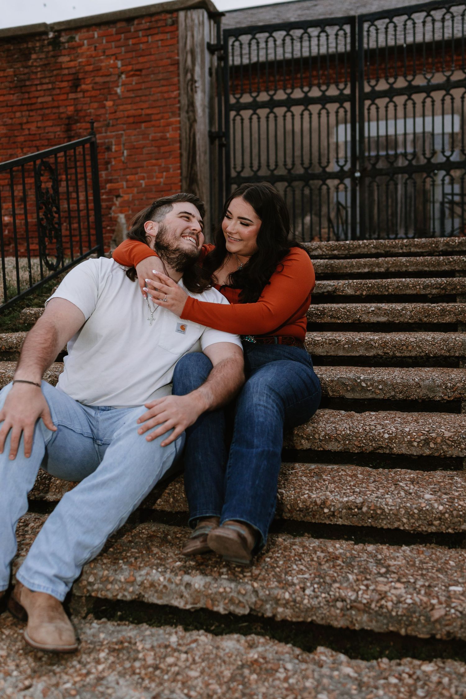 Happy couple sitting on outdoor stone steps, woman in orange top embracing man in white shirt and jeans.