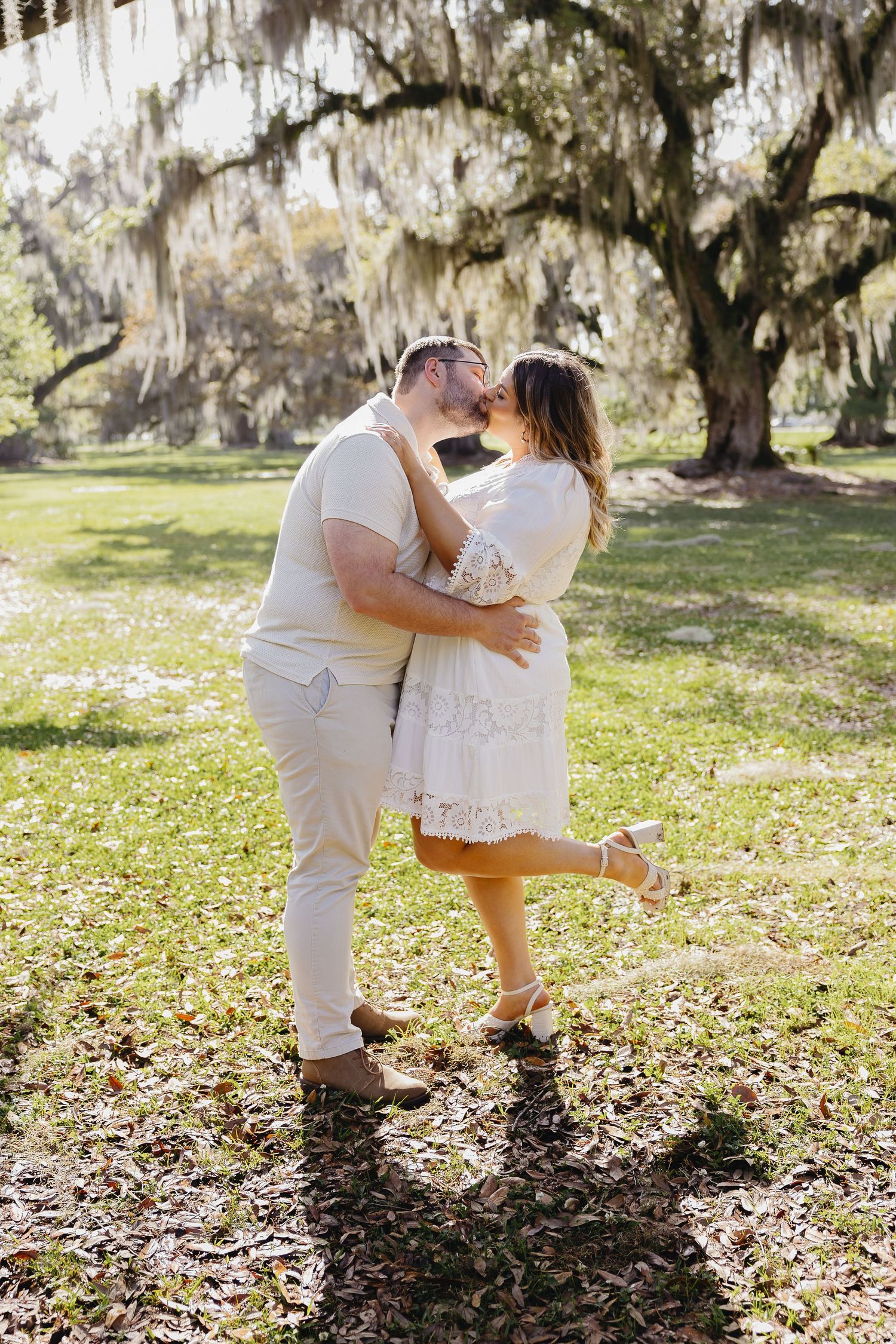 Couple sharing a romantic dip kiss under Spanish moss oak trees in sunny park.
