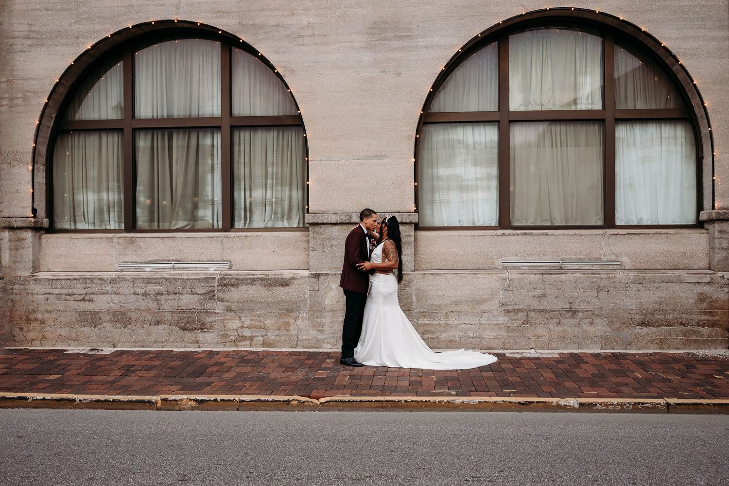 Wedding couple kissing against a stone building wall on a brick sidewalk.