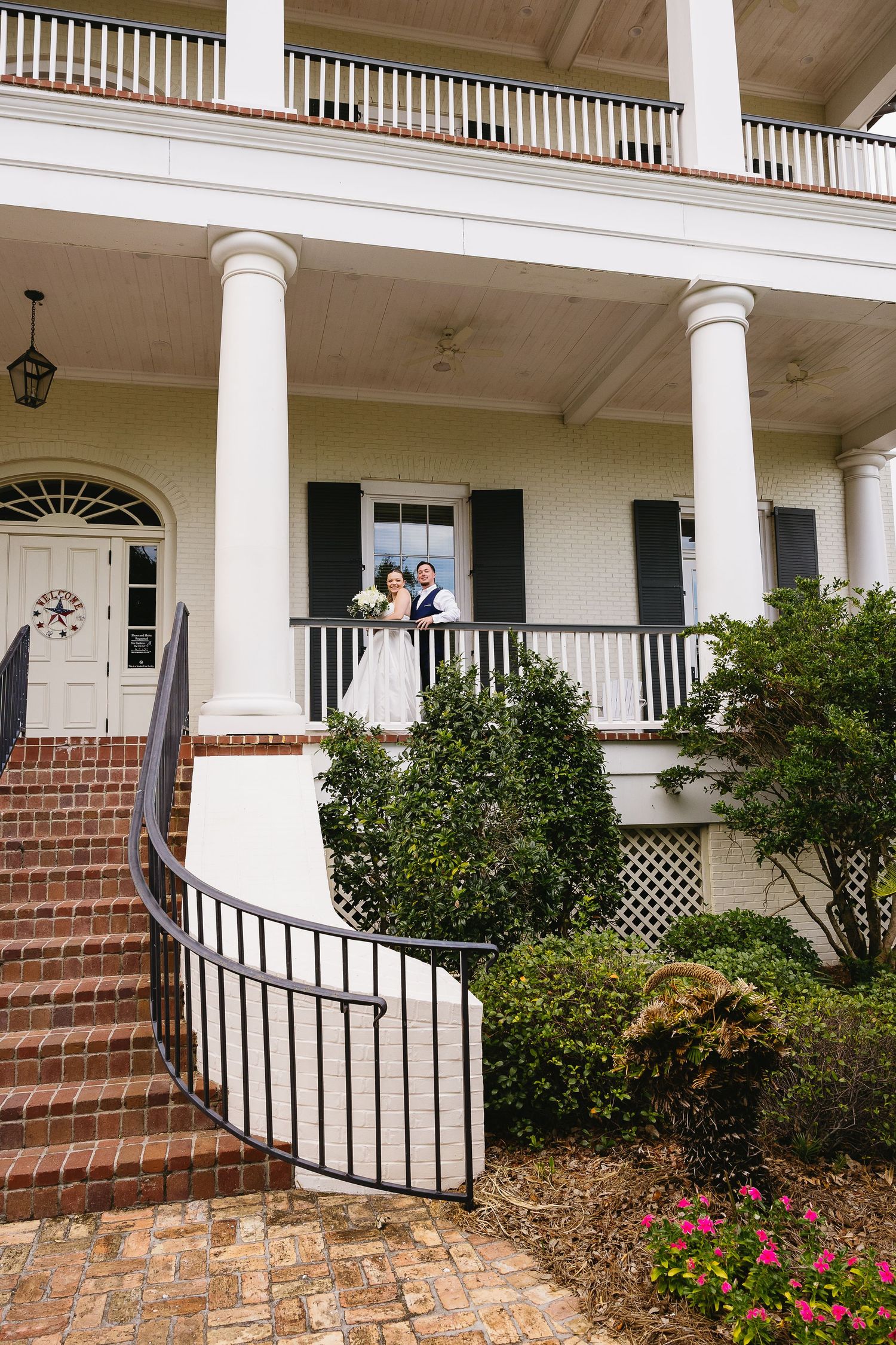 Bride and groom posing on the balcony of a stately white Southern colonial mansion.
