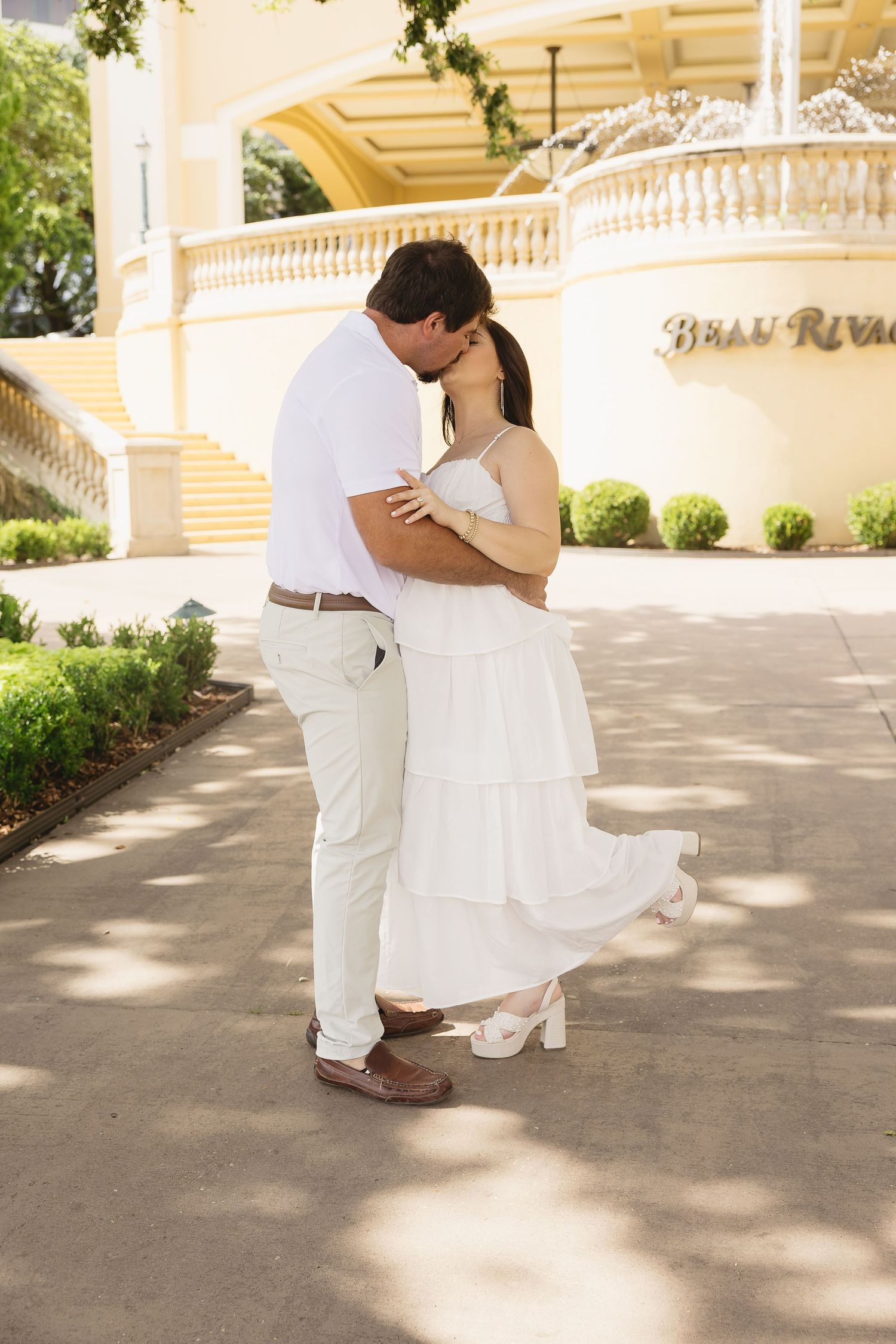 Couple sharing a kiss outside the Beau Rivage resort, woman in a flowing white maternity dress.