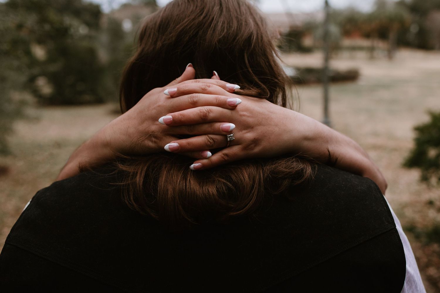 Close-up of a woman embracing someone, showcasing a sparkling engagement ring on her hand.