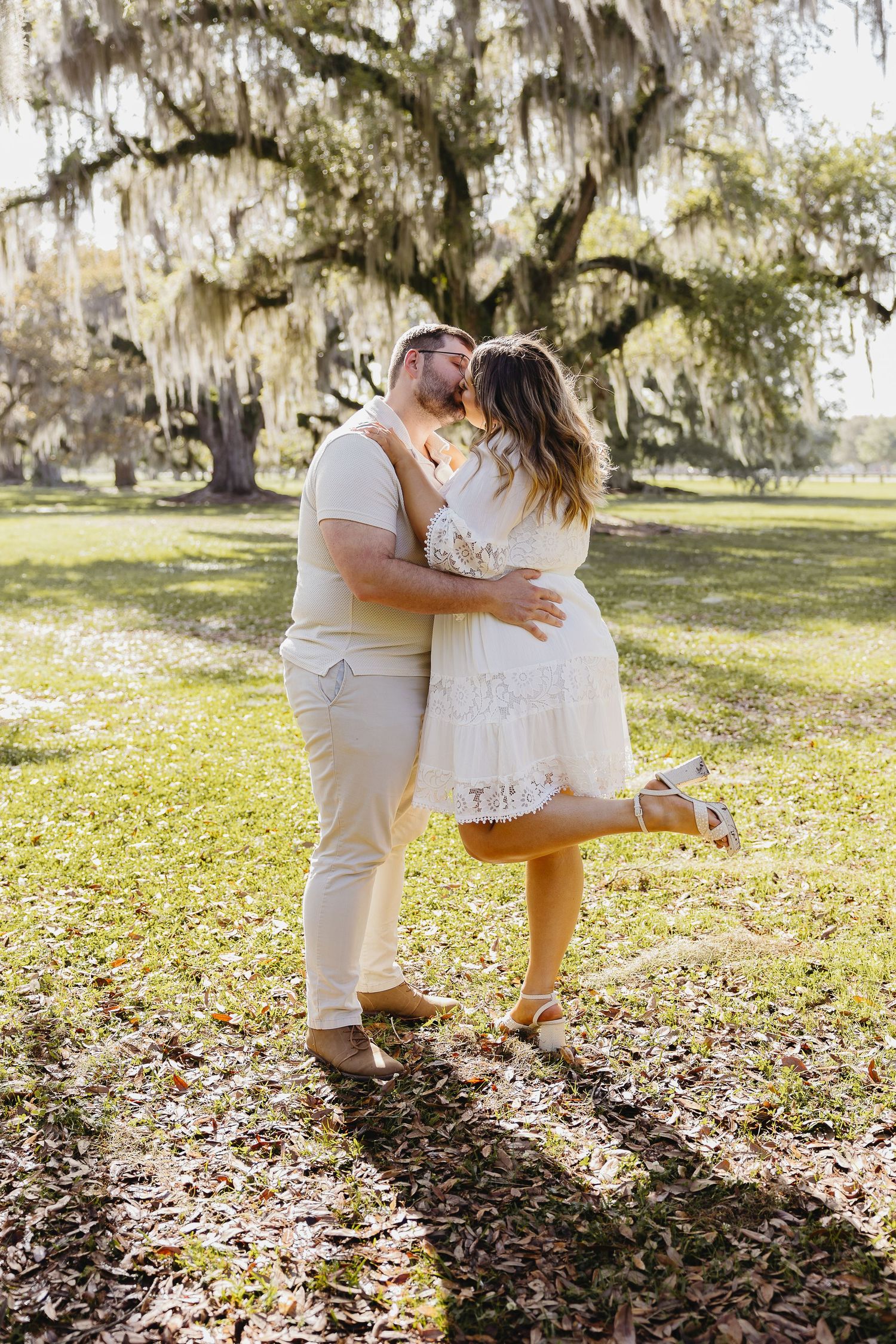 Couple sharing a romantic kiss under Spanish moss-draped oak tree in sunny park.