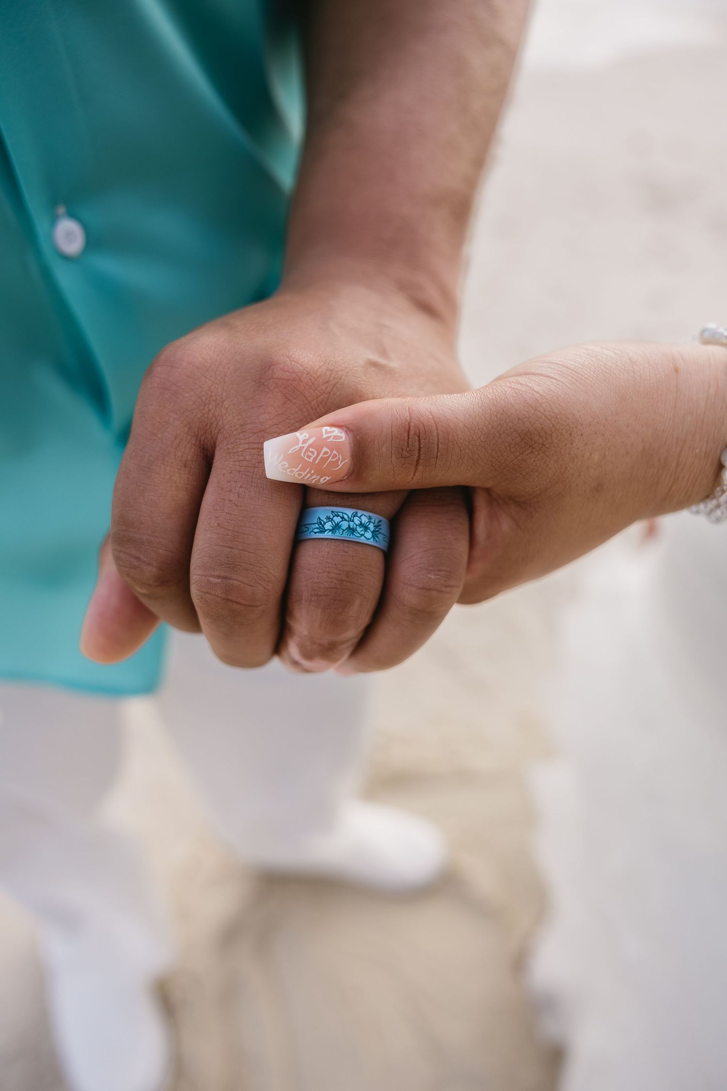 Close-up of newlyweds holding hands, groom wearing a blue turquoise wedding band ring.