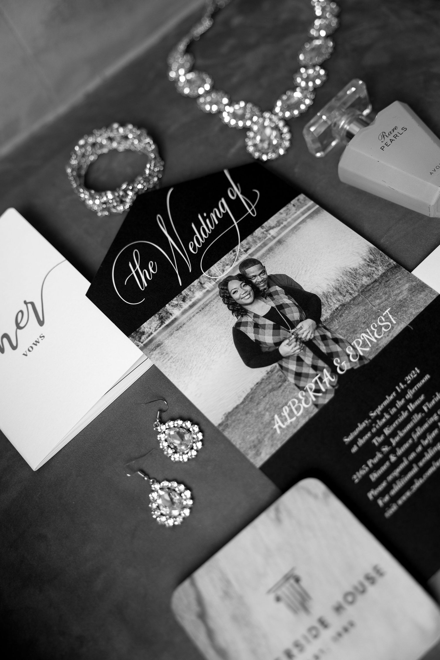 Black and white flat lay of wedding invitation, jewelry, and accessories for Alberta and Ernest.