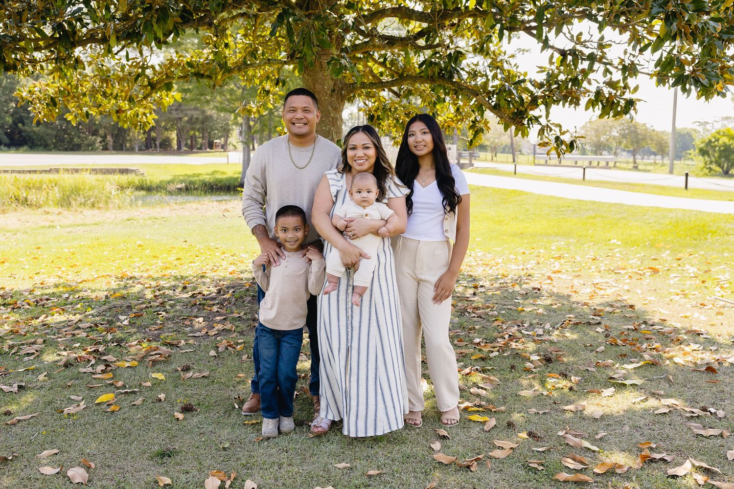 Happy Asian family of five posing under a tree in a park during fall season.