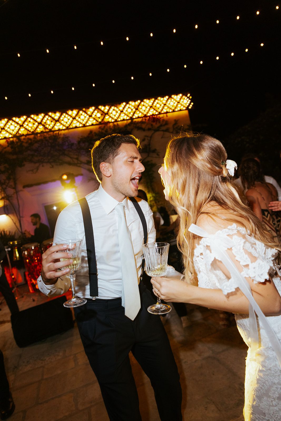 A couple shares a joyful dance moment together at an evening wedding reception under twinkling lights.