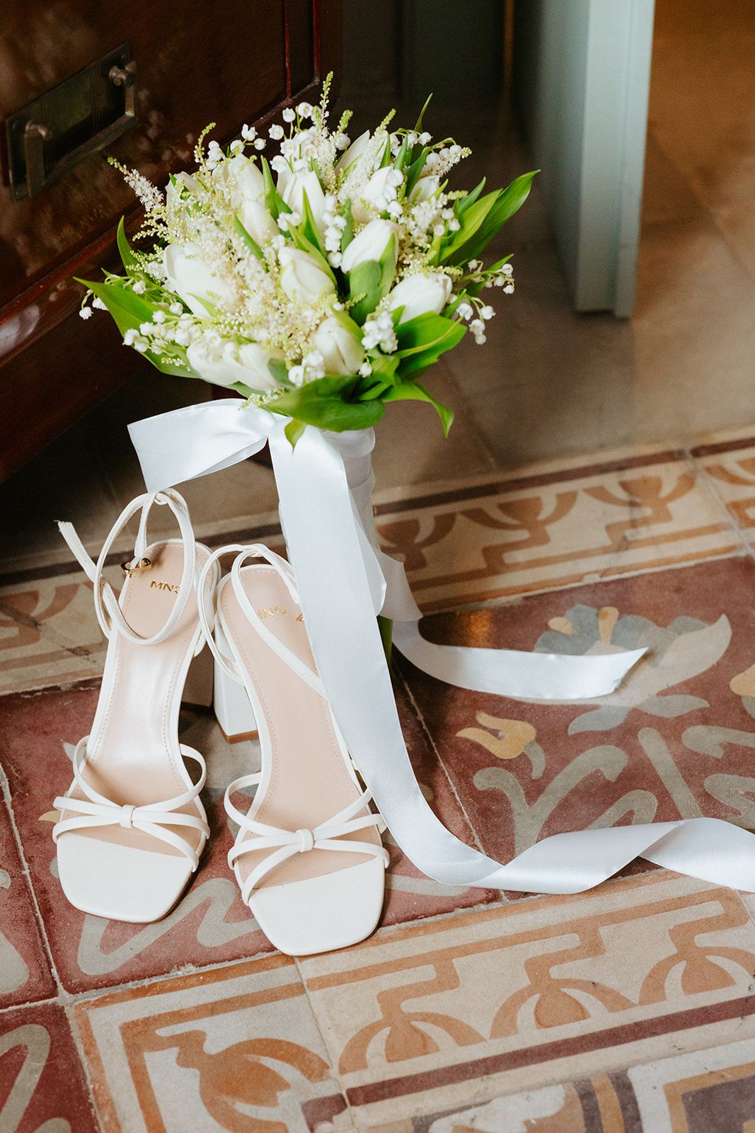 White bridal shoes and floral bouquets arranged on a decorative tiled floor for a wedding photoshoot.