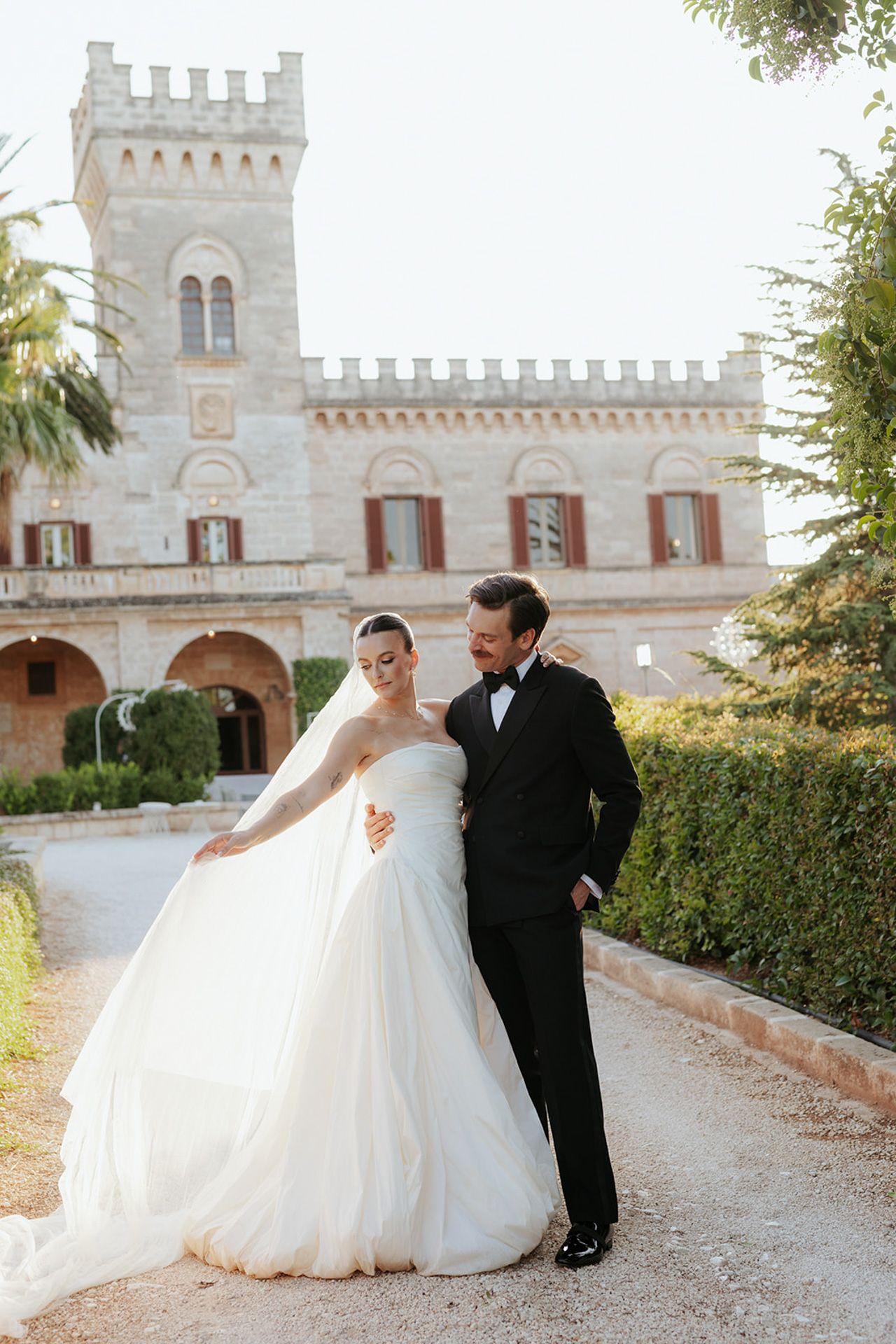 A romantic wedding photo series showing a couple posing in front of a majestic castle with white stone walls.