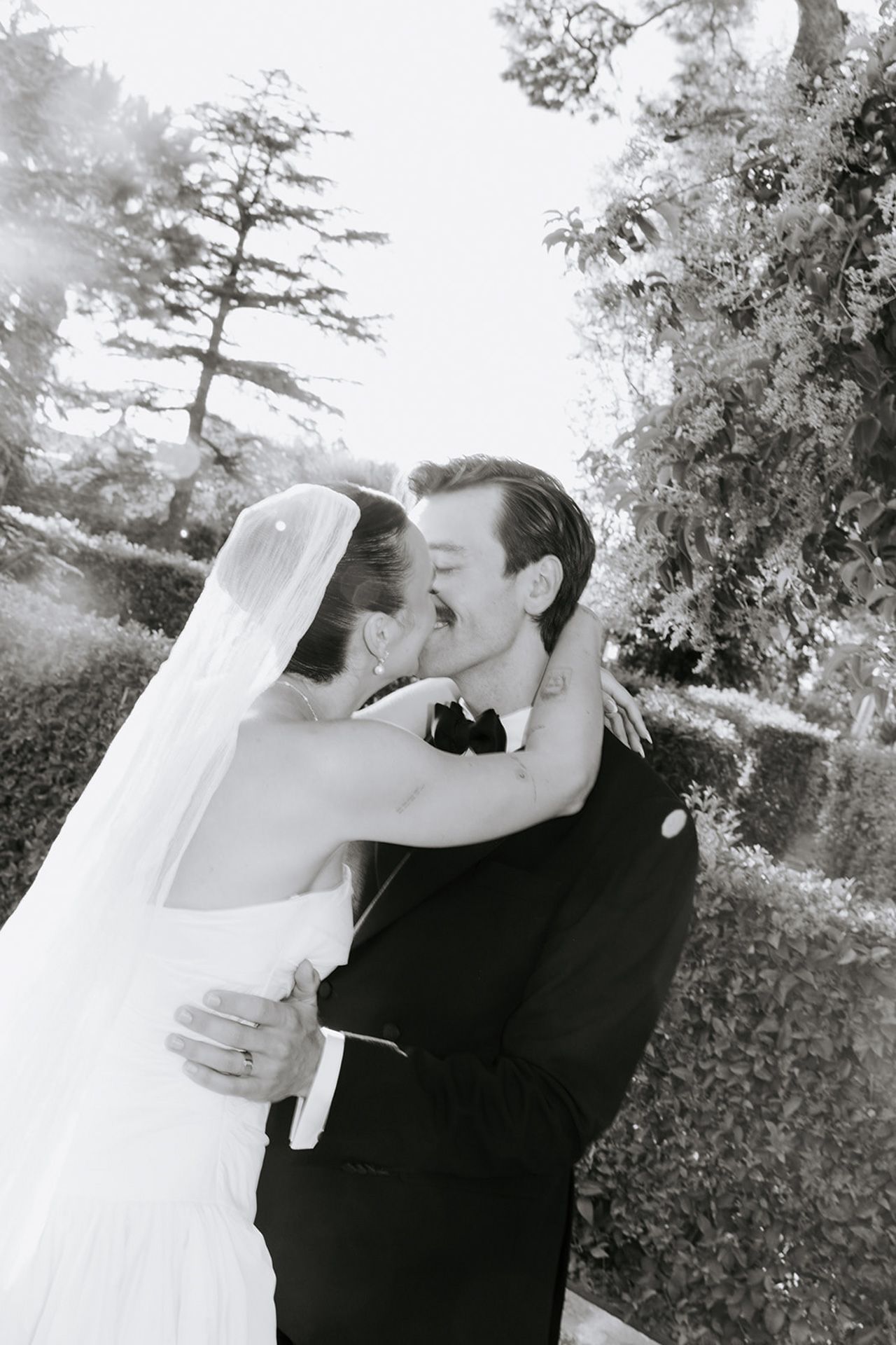 A romantic black and white wedding photo series showing a couple sharing intimate kisses in an outdoor garden setting.