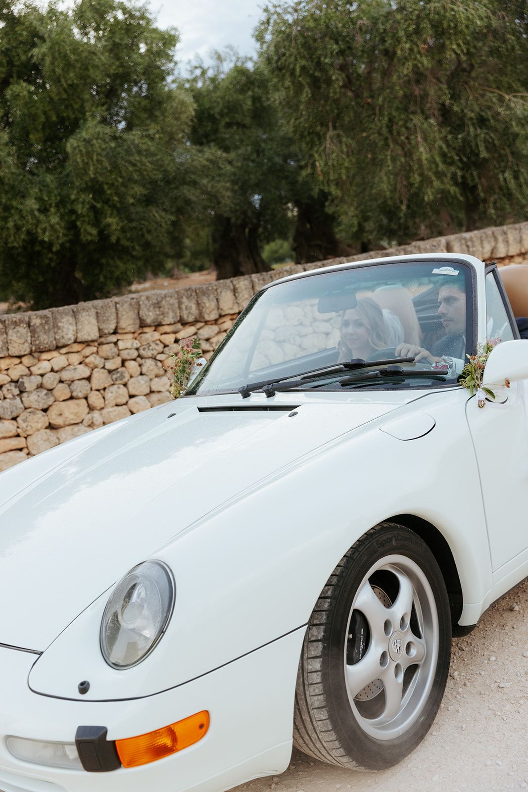 White classic Porsche convertible sports car shown from various front angles against stone wall backdrop.
