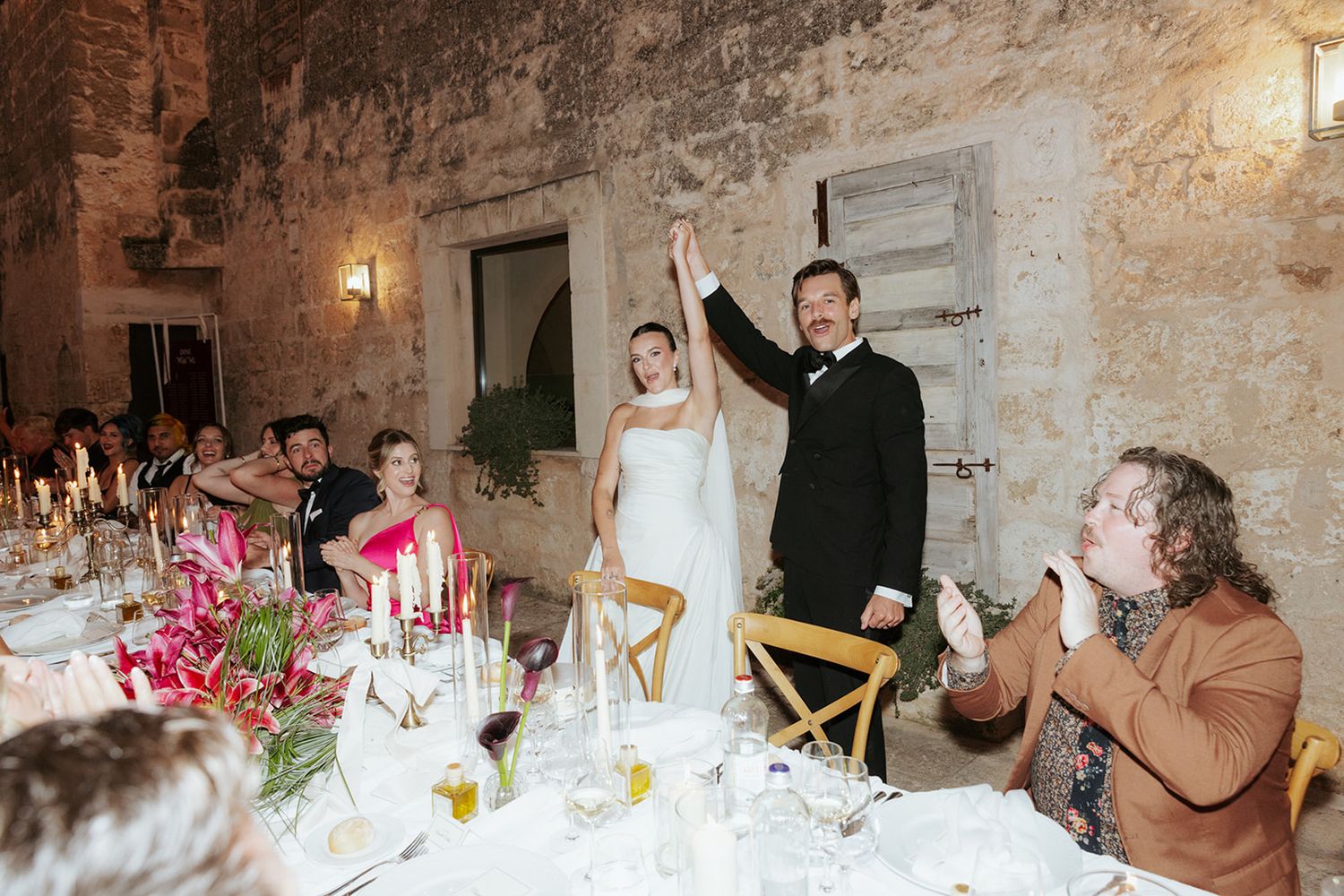 Wedding guests enjoying an intimate dinner reception in a rustic stone-walled venue with warm lighting and elegant table settings.