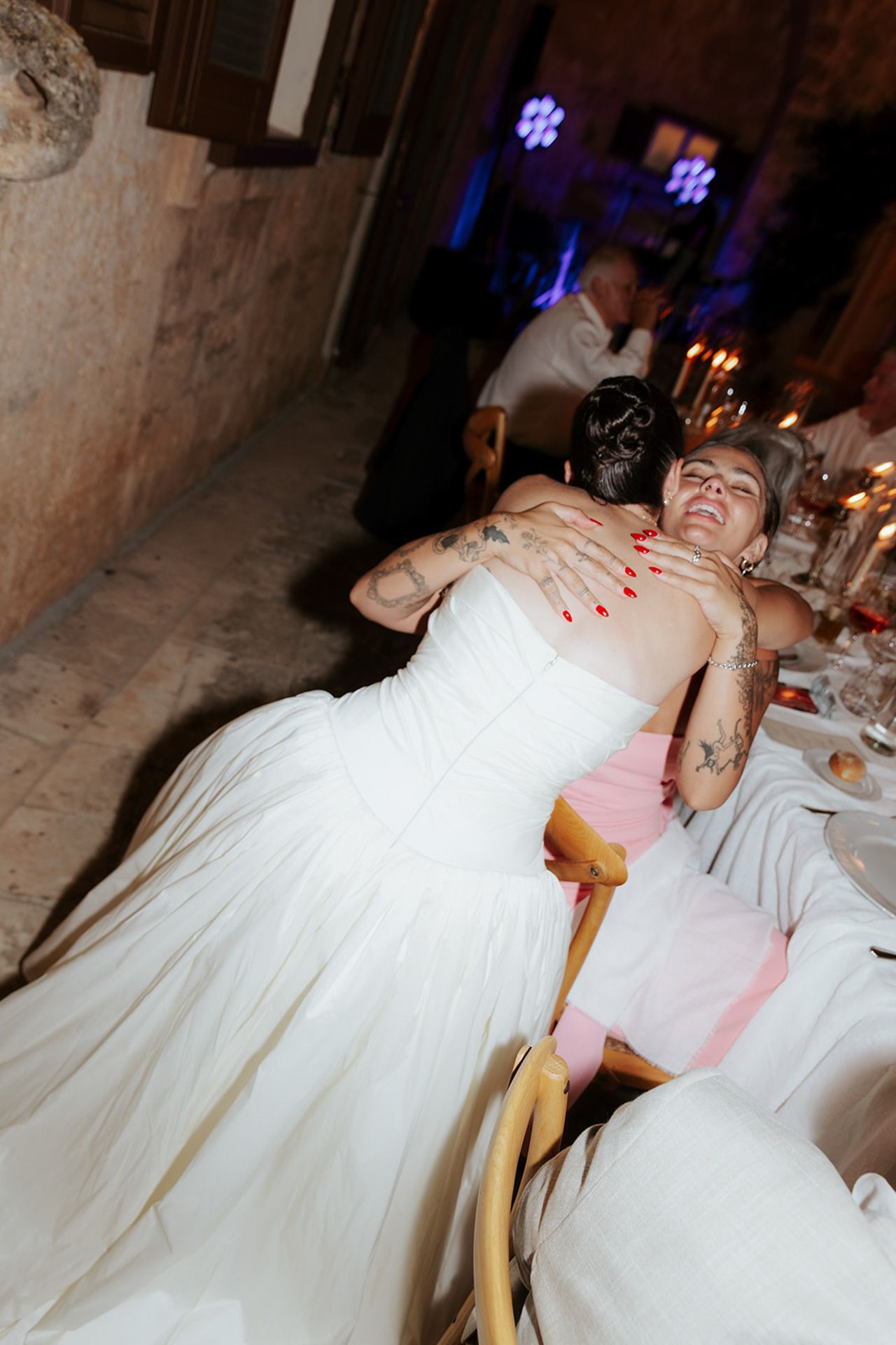 A bride in a white wedding dress laughs joyfully while seated at a reception dinner table.