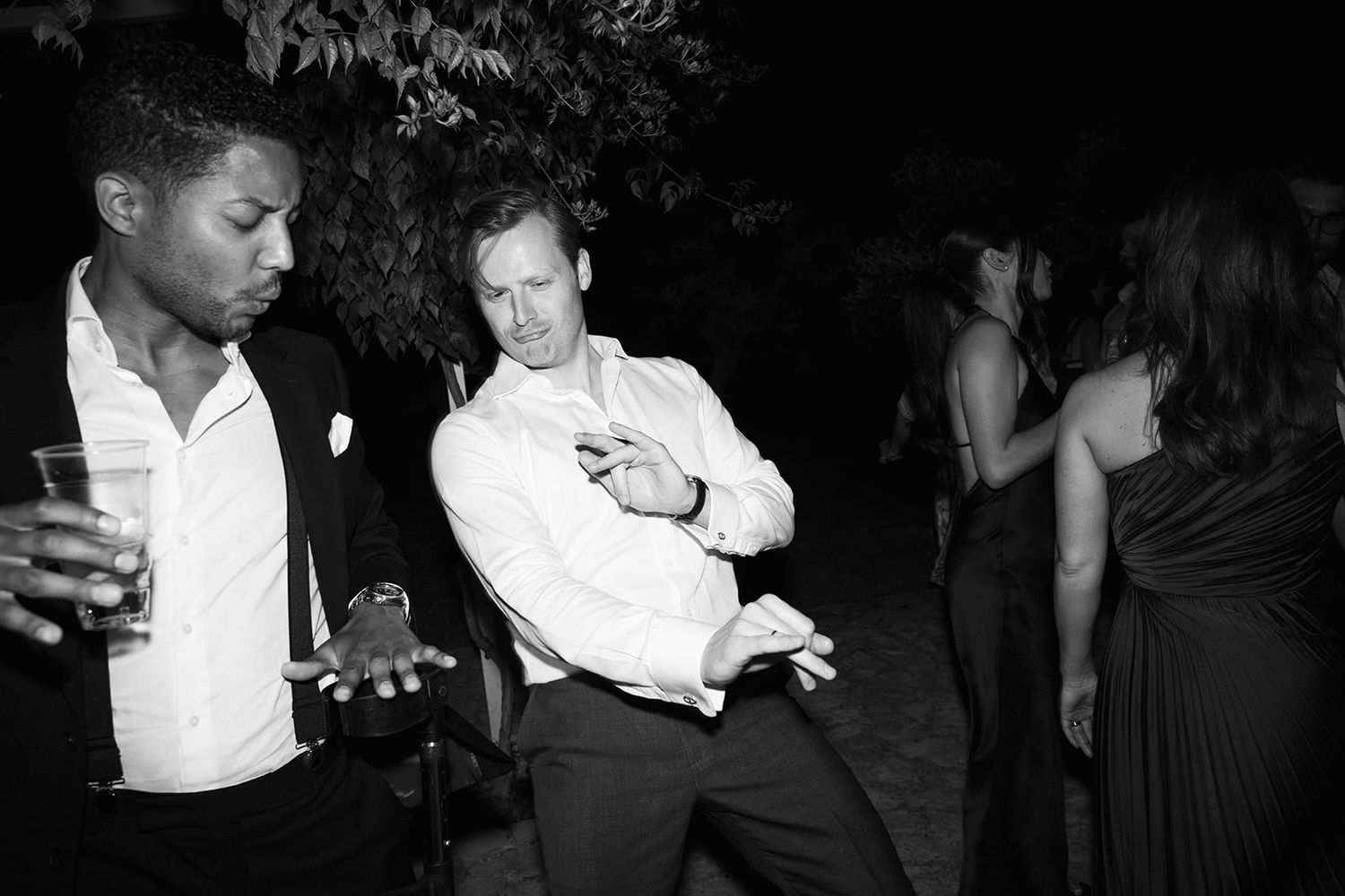 Two people dancing at a nighttime party, with one in a white shirt showing off dance moves in black and white photography.