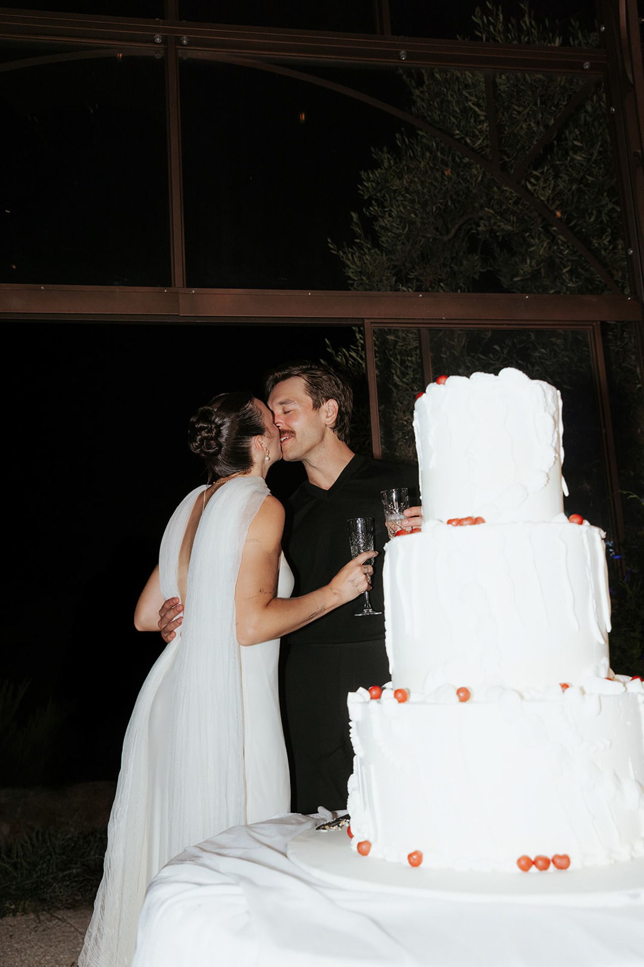 Newlyweds share a romantic moment while cutting their elegant white wedding cake adorned with small orange decorations.