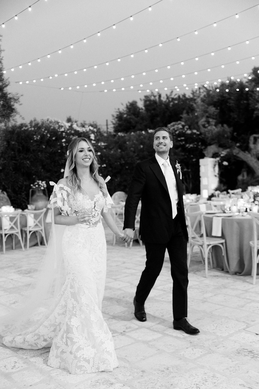 A couple dances together on an outdoor patio with string lights overhead during an evening wedding reception.