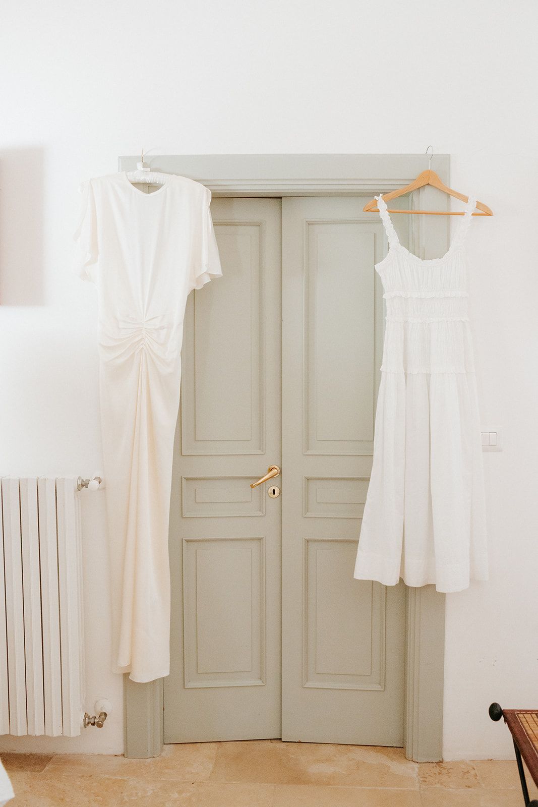 A collection of white dresses and garments hanging on wooden hangers against a light gray wall.
