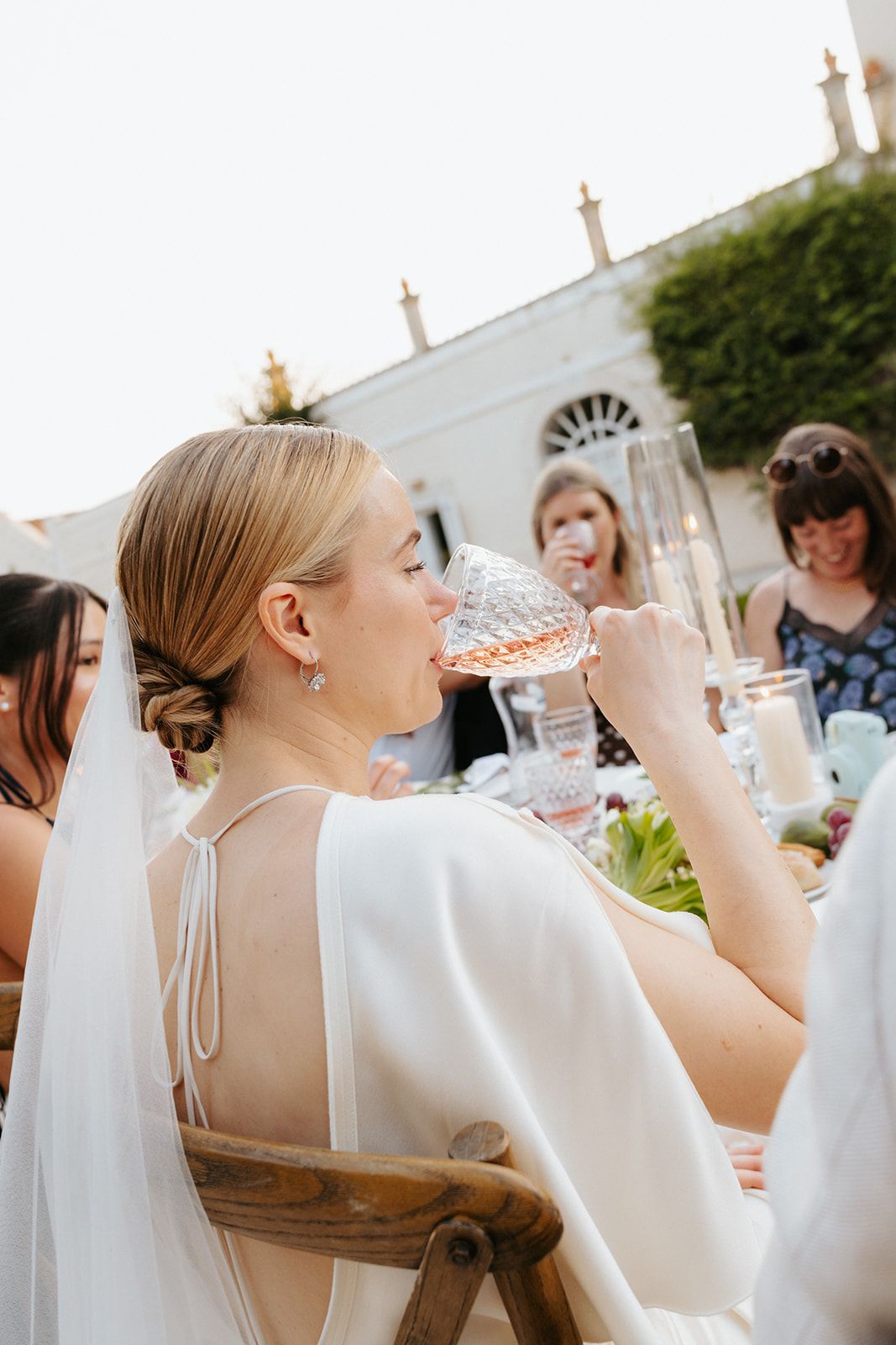 A person in a white wedding dress drinking from a glass during an outdoor reception celebration.
