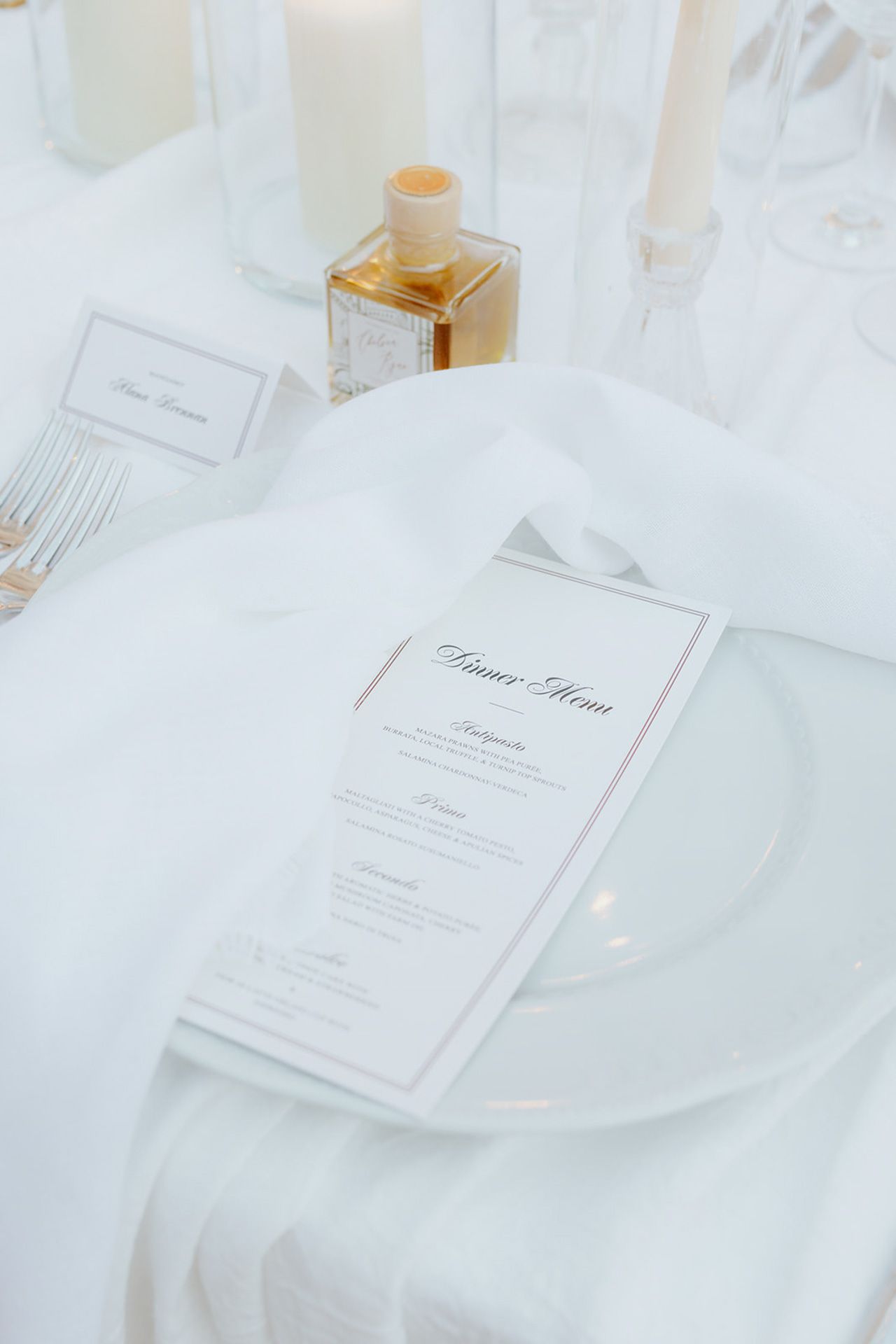 Close-up of minimalist white place settings with menu cards and delicate tableware.