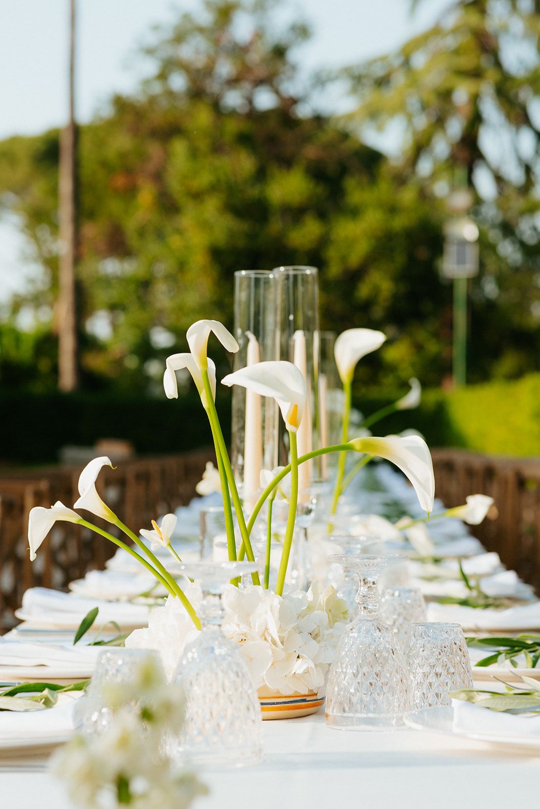 Elegant outdoor wedding table setting with white calla lilies and crystal glassware in a garden setting.