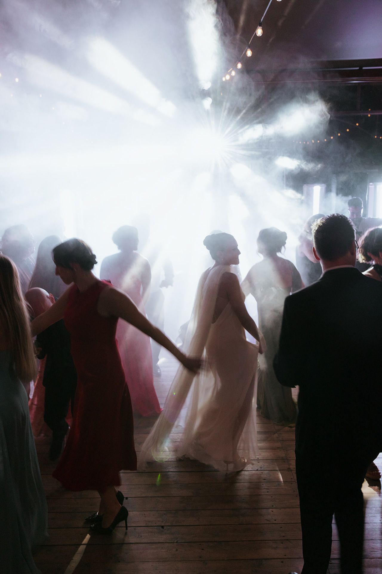 Silhouettes of people dancing in a smoky nightclub with dramatic white stage lighting creating an atmospheric ambiance.
