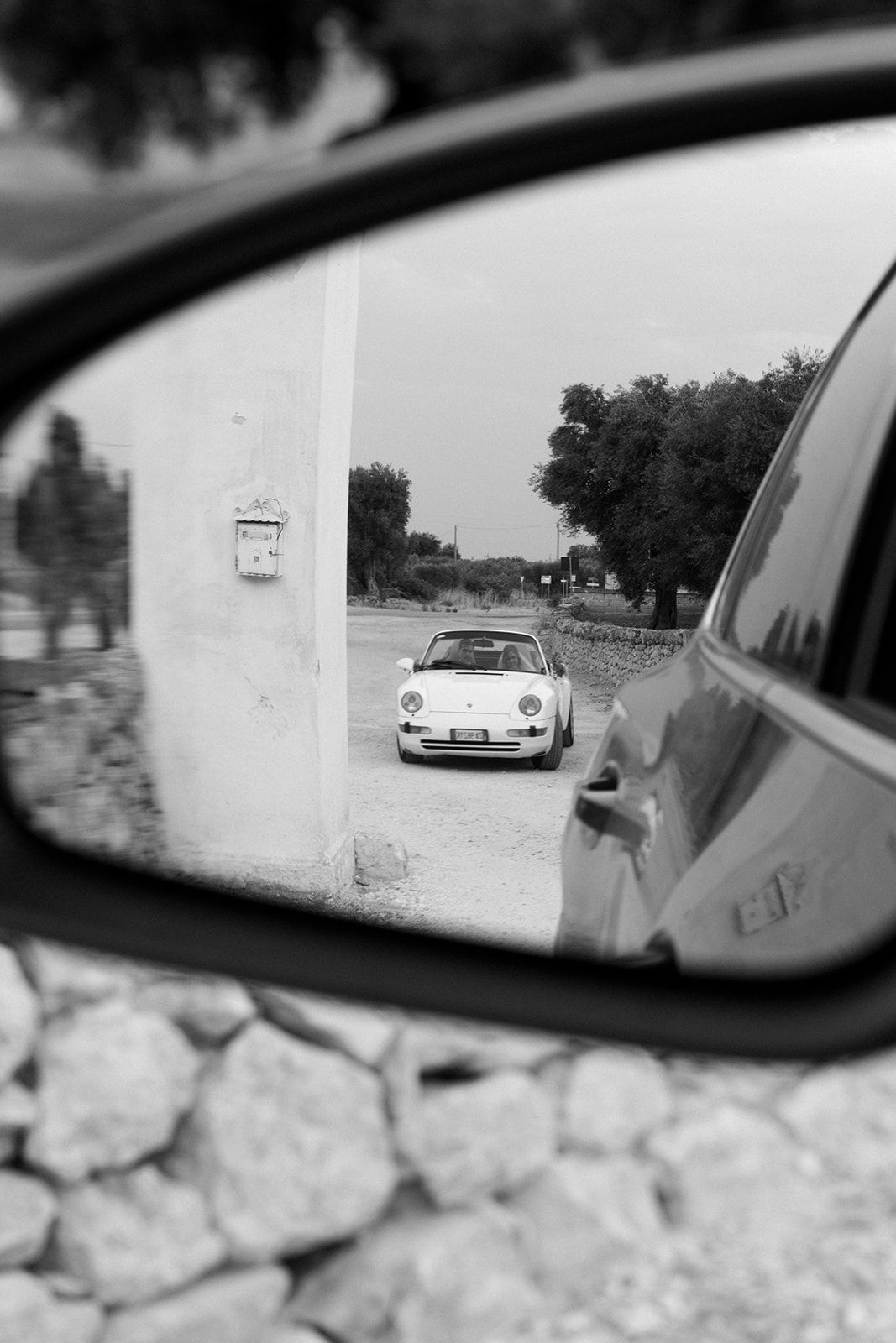 Black and white series of side mirror reflections showing a vintage Porsche 911 following on a scenic road.
