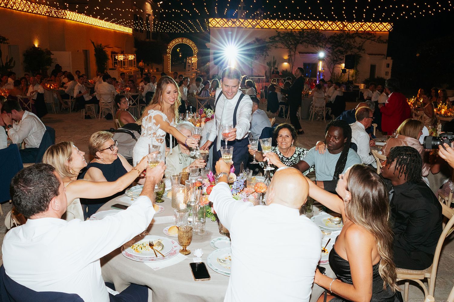 Wedding reception guests enjoying dinner and conversation at decorated tables in a dimly lit venue.