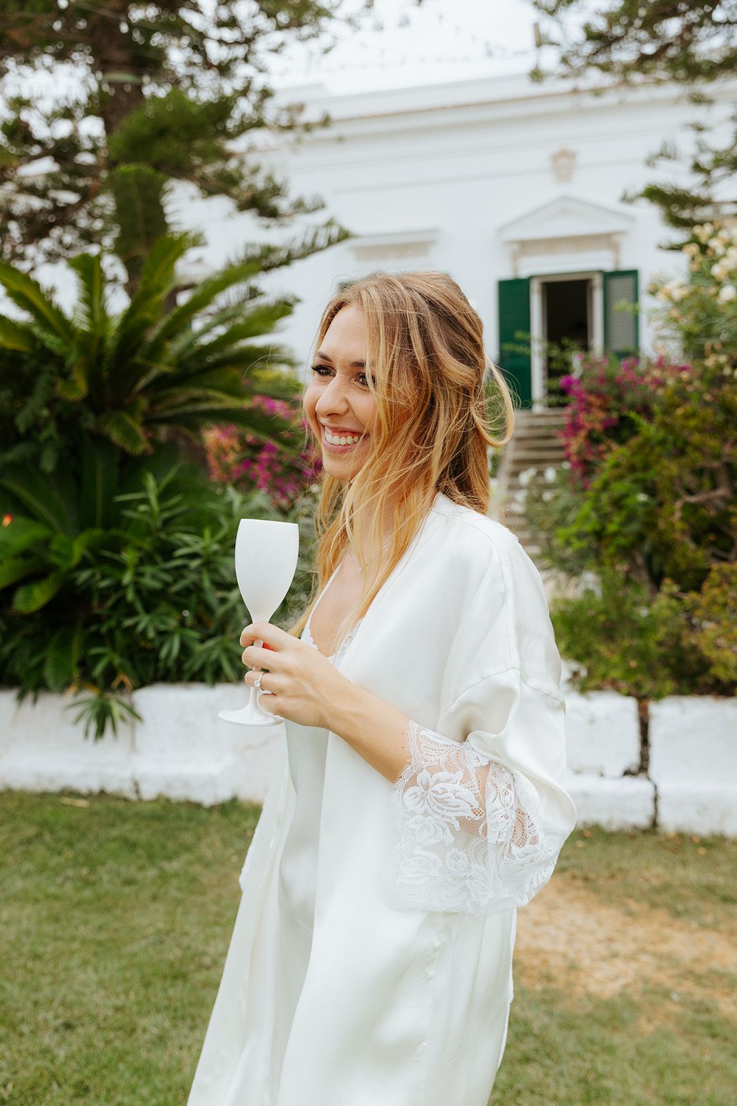 A person in a flowing white dress spins joyfully in a garden setting with greenery and white walls in the background.