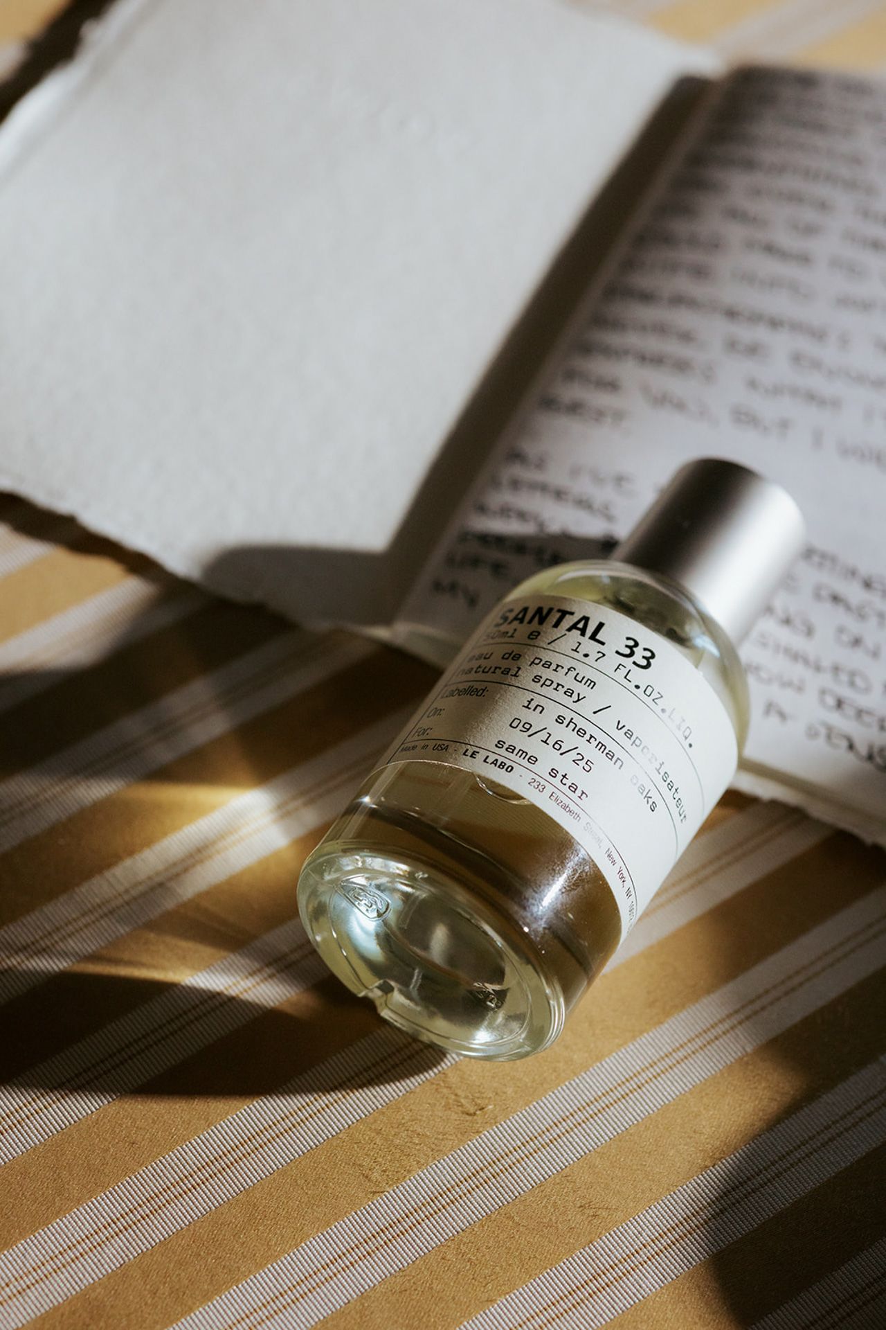 A small glass vial or medicine bottle casts dramatic shadows across an open book page in natural lighting.