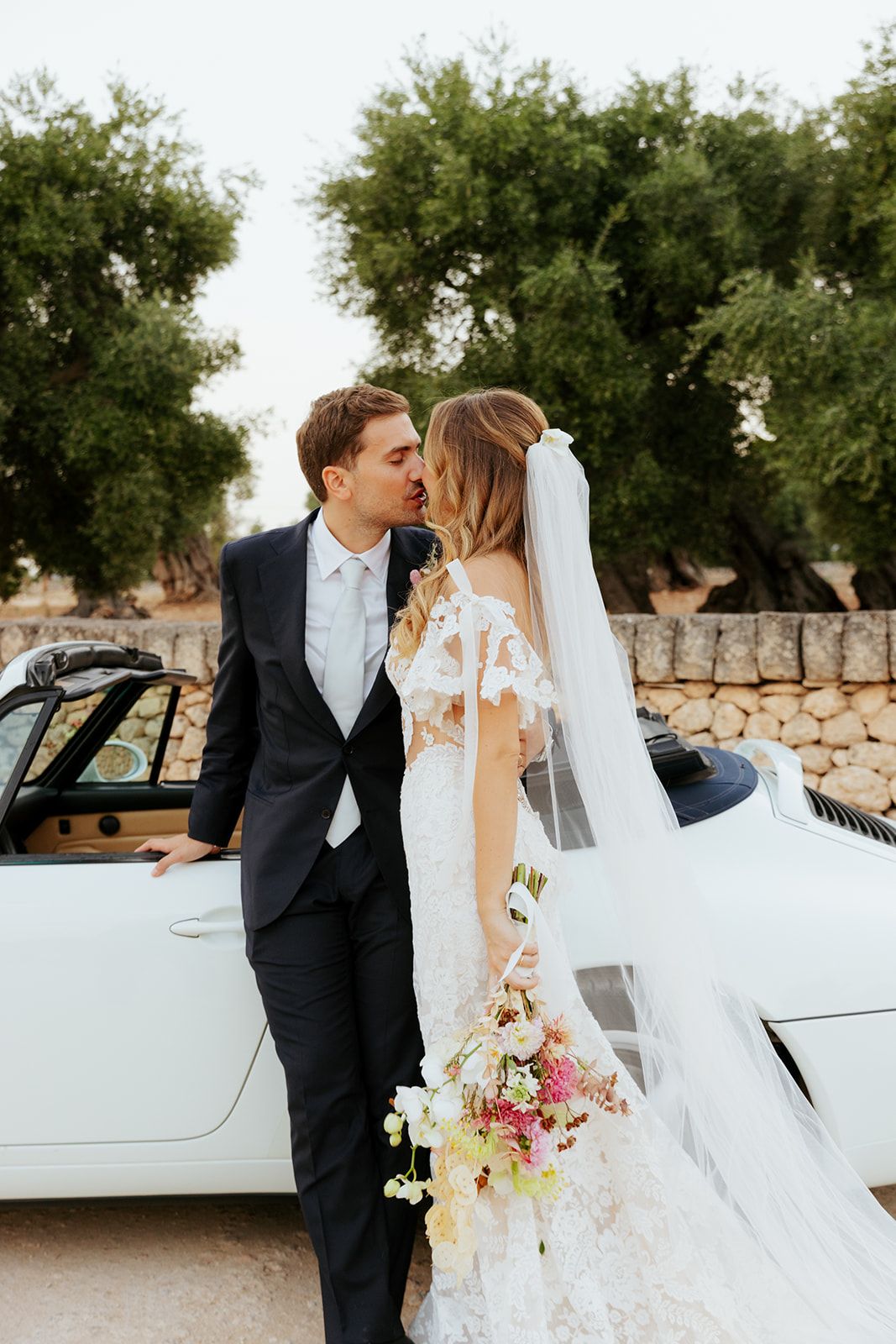 Romantic wedding couple poses with vintage light blue classic car on their special day.