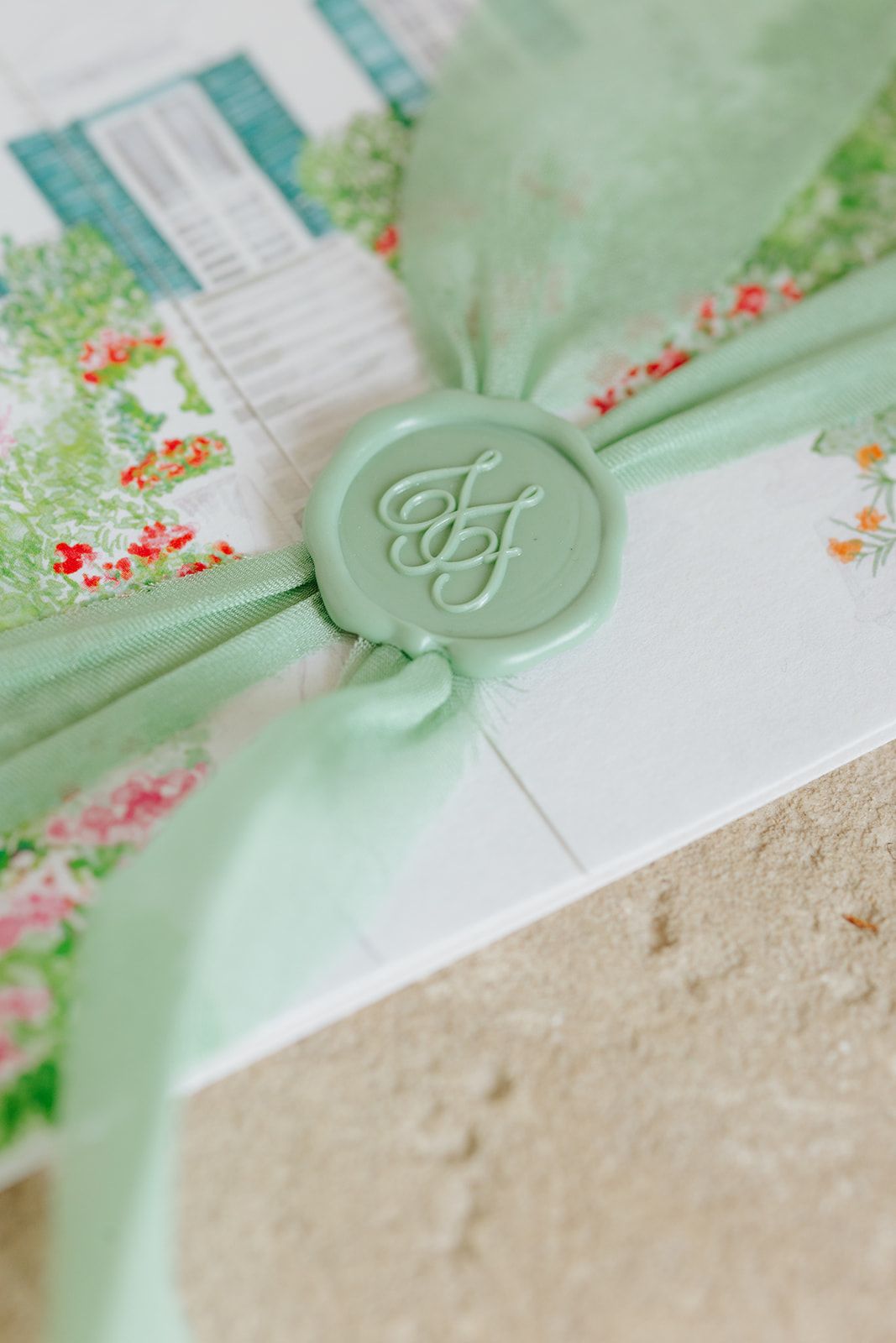 Close-up view of mint green wax seals and delicate floral stationery details on a white background.