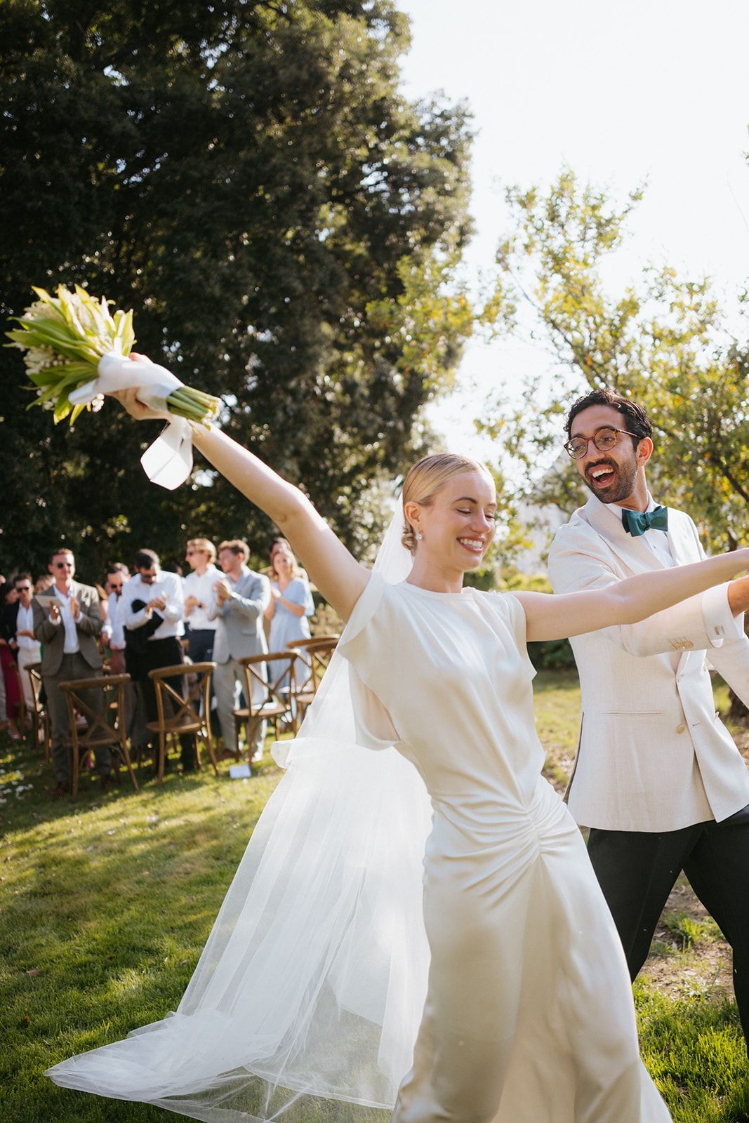 Candid moments of joyful newlyweds dancing and twirling together in bright sunlight surrounded by guests during their outdoor wedding.