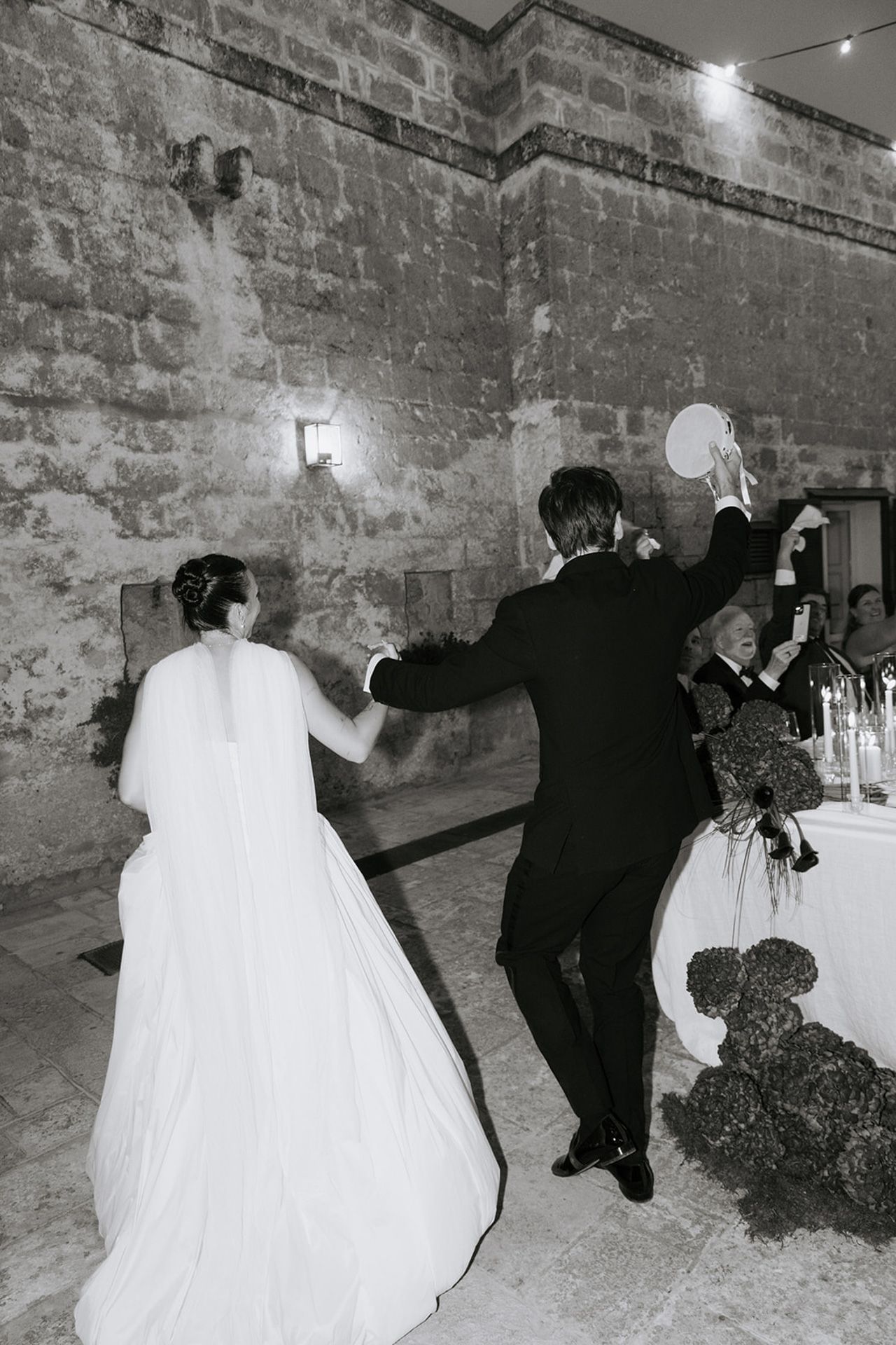 A sequence of wedding party members performing a synchronized dance move in a rustic brick-walled venue.