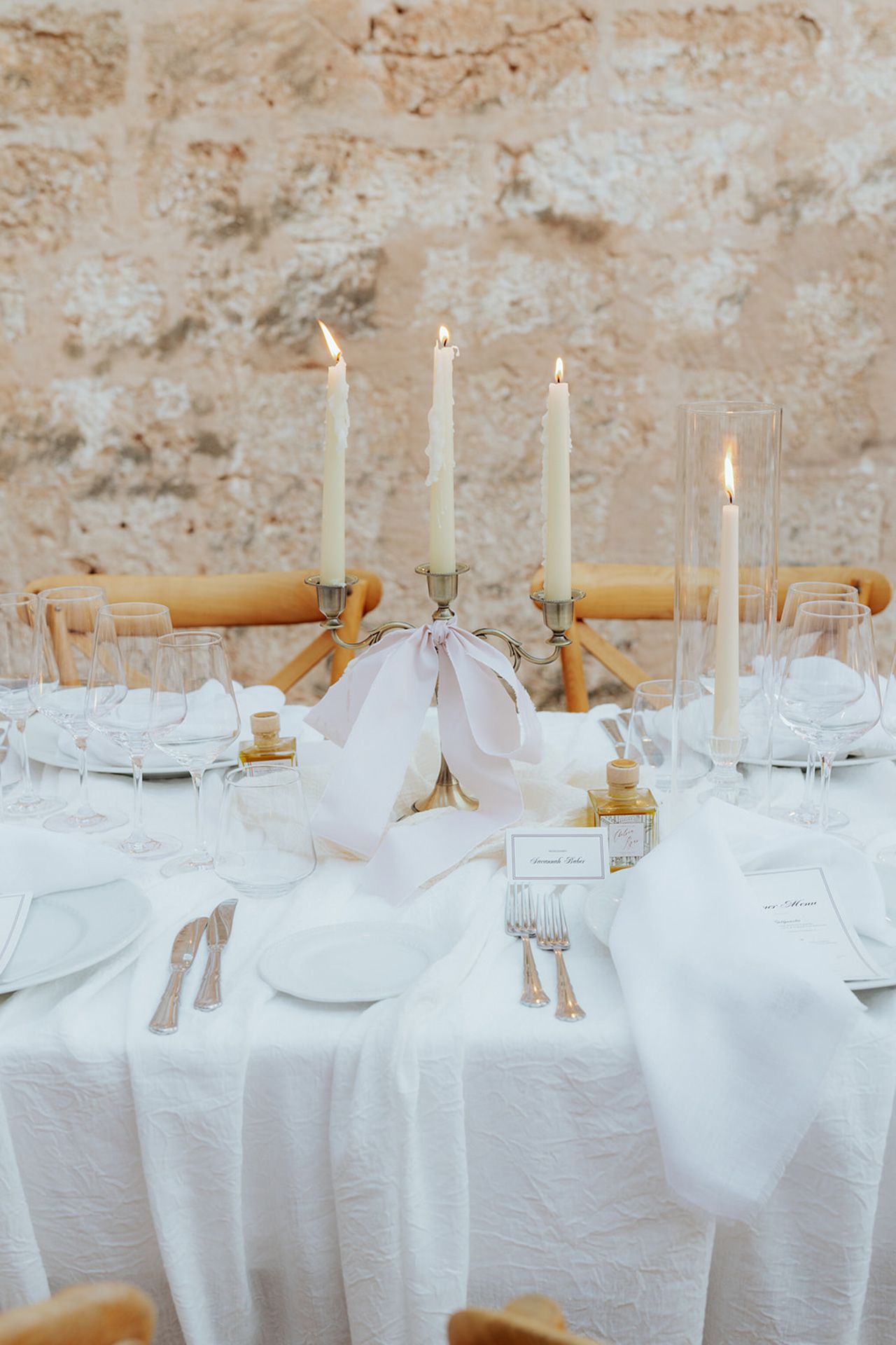 White tablecloths and tall candles create an elegant dining atmosphere against a rustic stone wall.