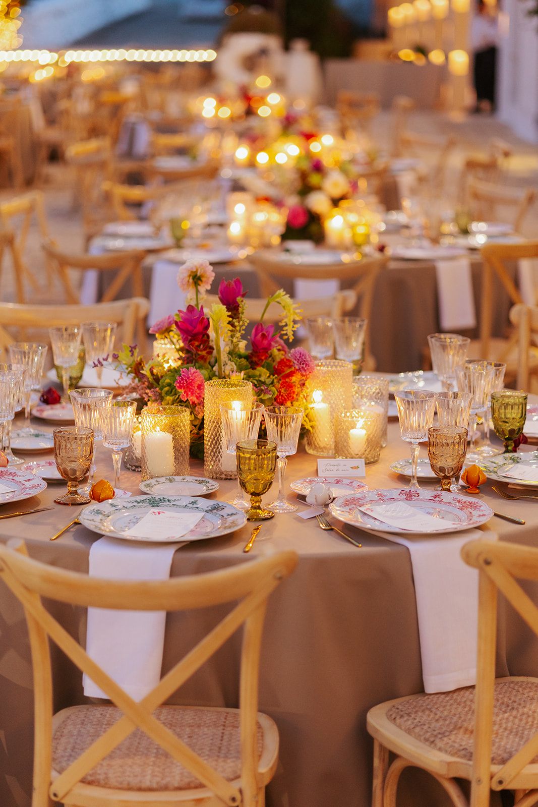 Elegant wedding reception table settings with glowing candlelight, pink floral centerpieces and cross-back wooden chairs.