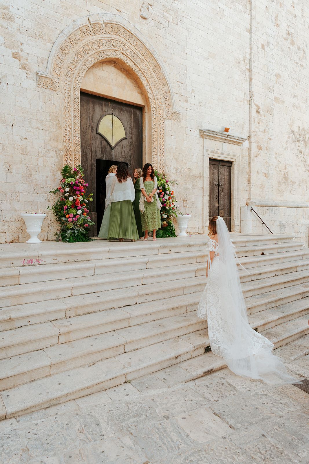 Wedding ceremony steps leading to historic stone church entrance decorated with floral arrangements and green decor.