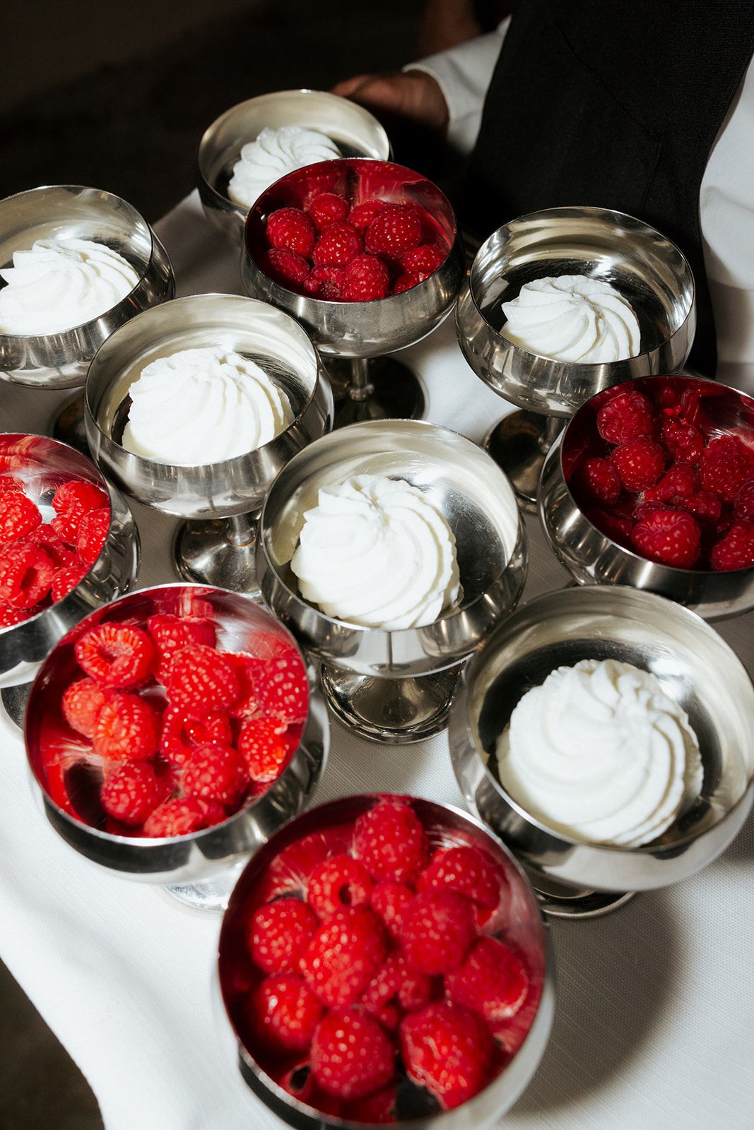 Silver bowls filled alternately with fresh red raspberries and white whipped cream for dessert service.