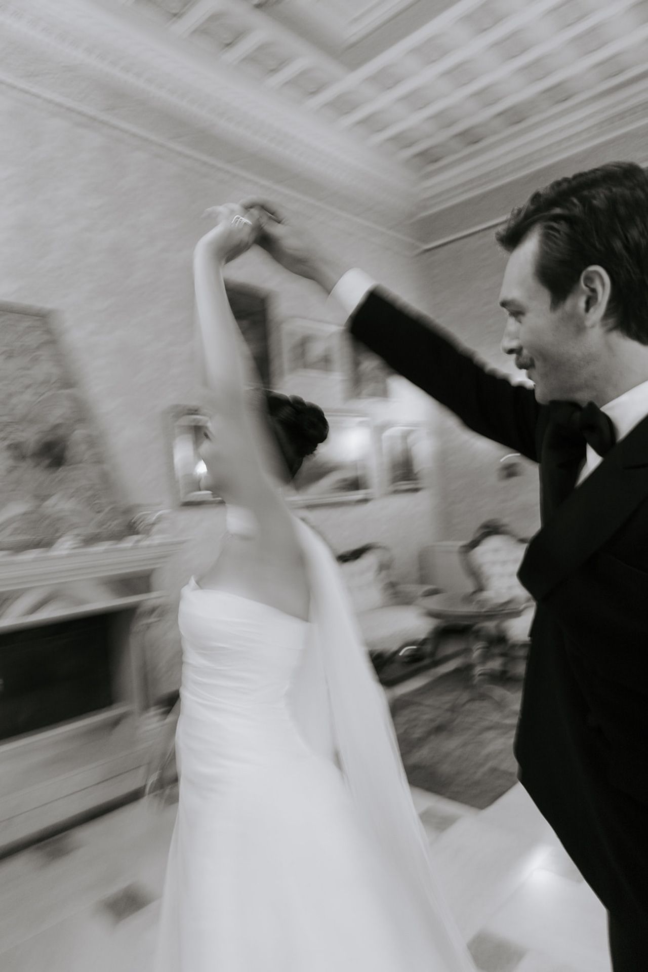 Motion blur captures a bride and groom dancing at their wedding reception in an elegant white room.