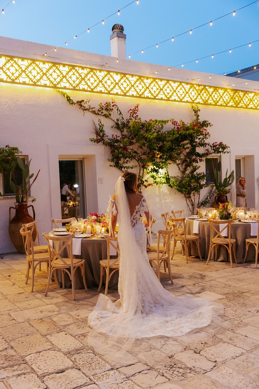 White-walled courtyard wedding venue decorated with string lights and wooden furniture for an evening reception.